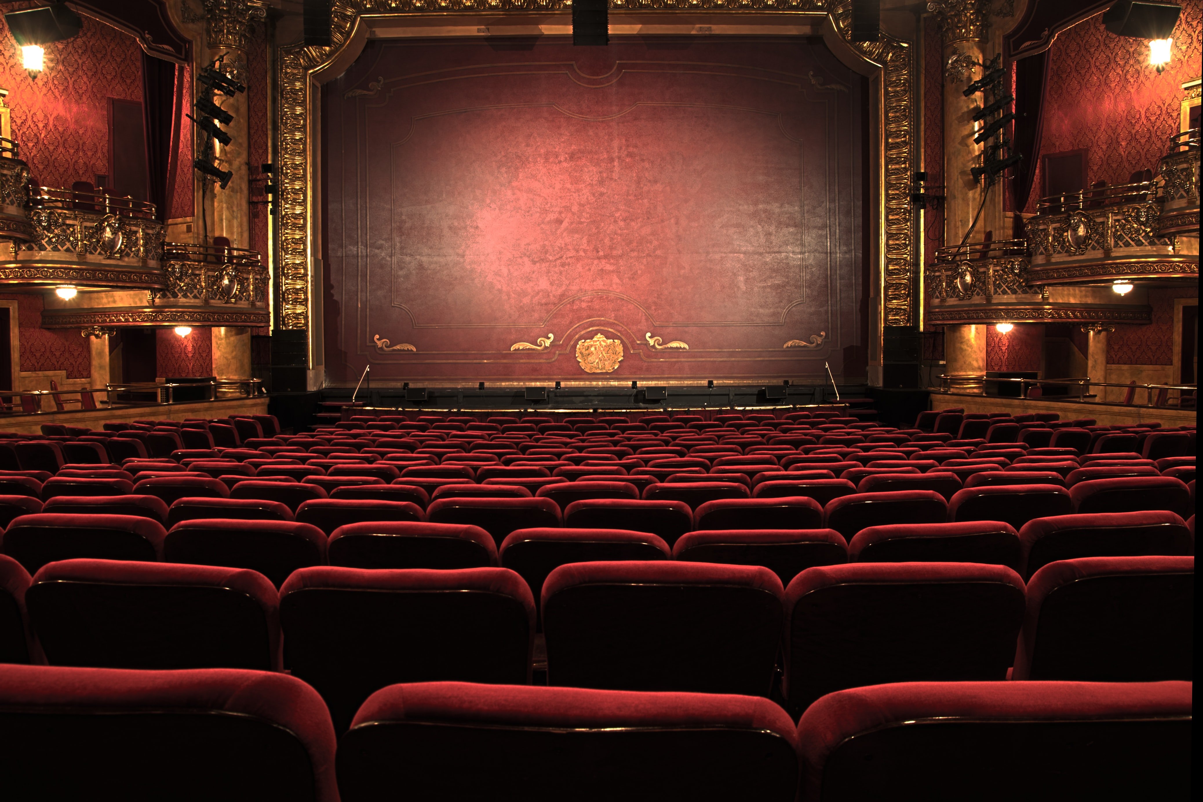 An ornate theatre with red chairs and stage curtain.