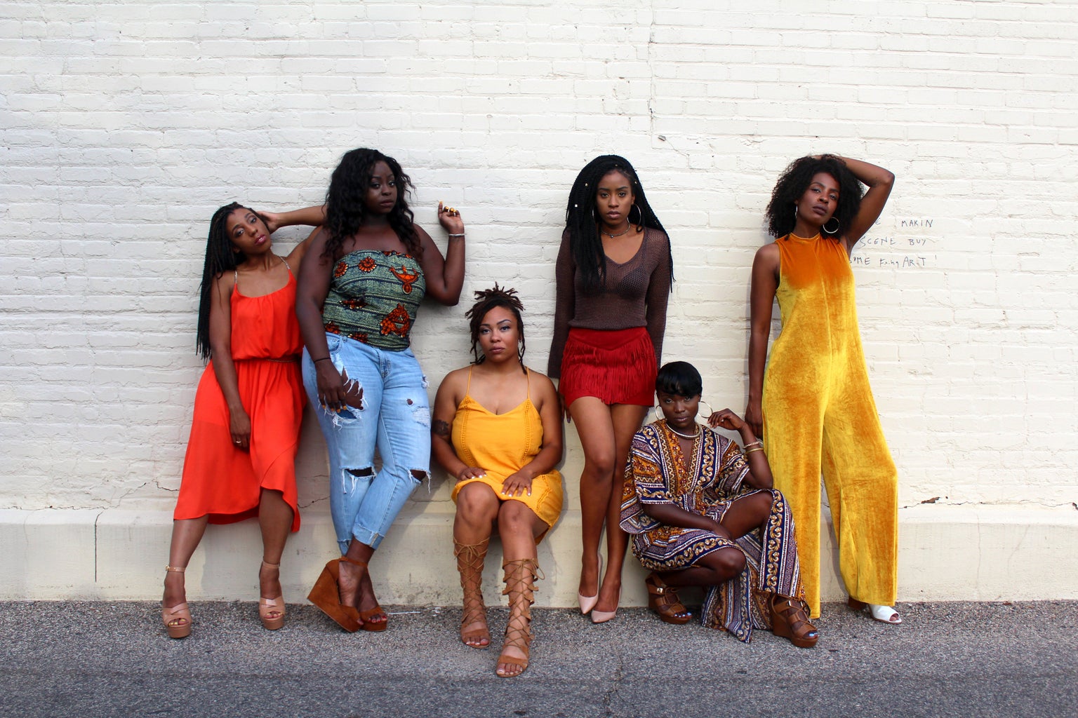 six black women standing and sitting agaisnt a white wall