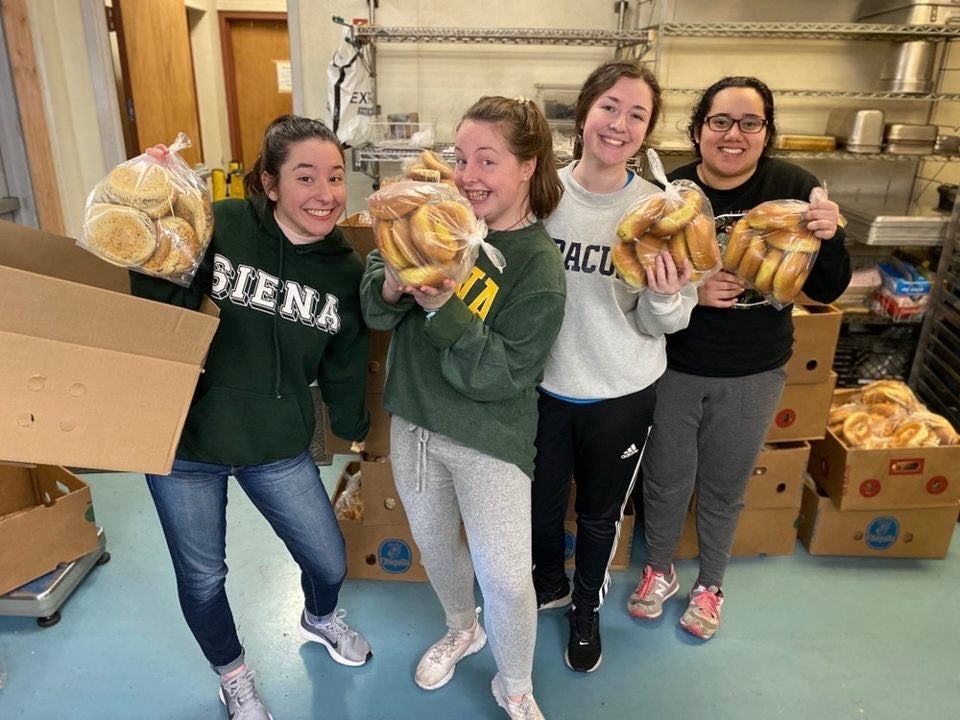 group of girls holding up bags of bagels