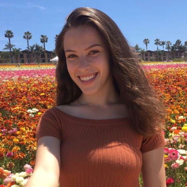 girl standing in front of a field of flowers, wearing an orange shirt