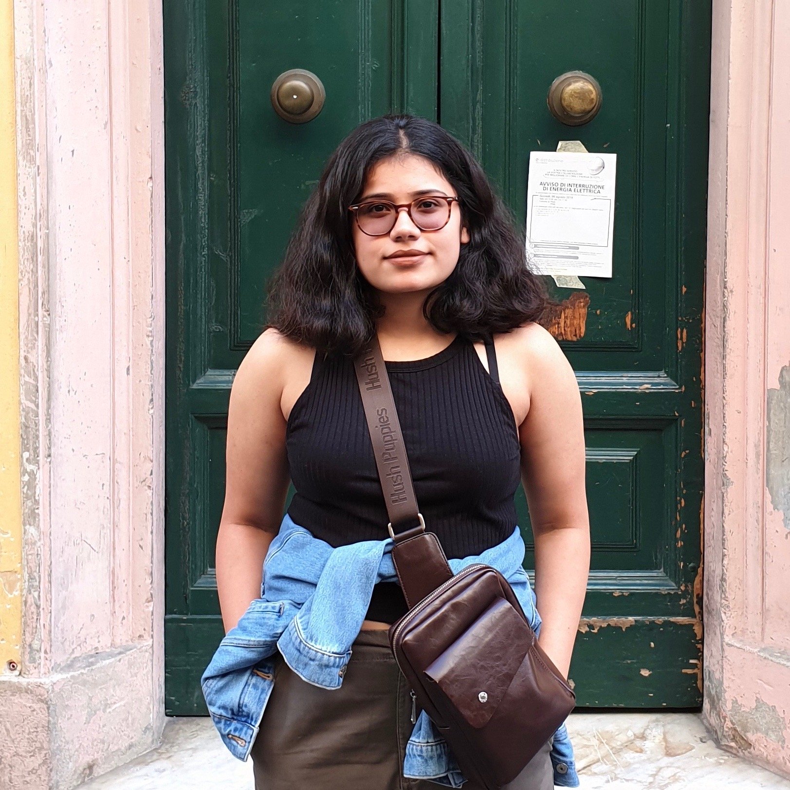 girl with short black hair and glasses standing in front of a green door