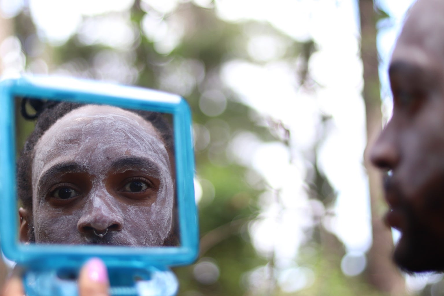 A Xhosa man, wearing traditional face paint, looks in a mirror.