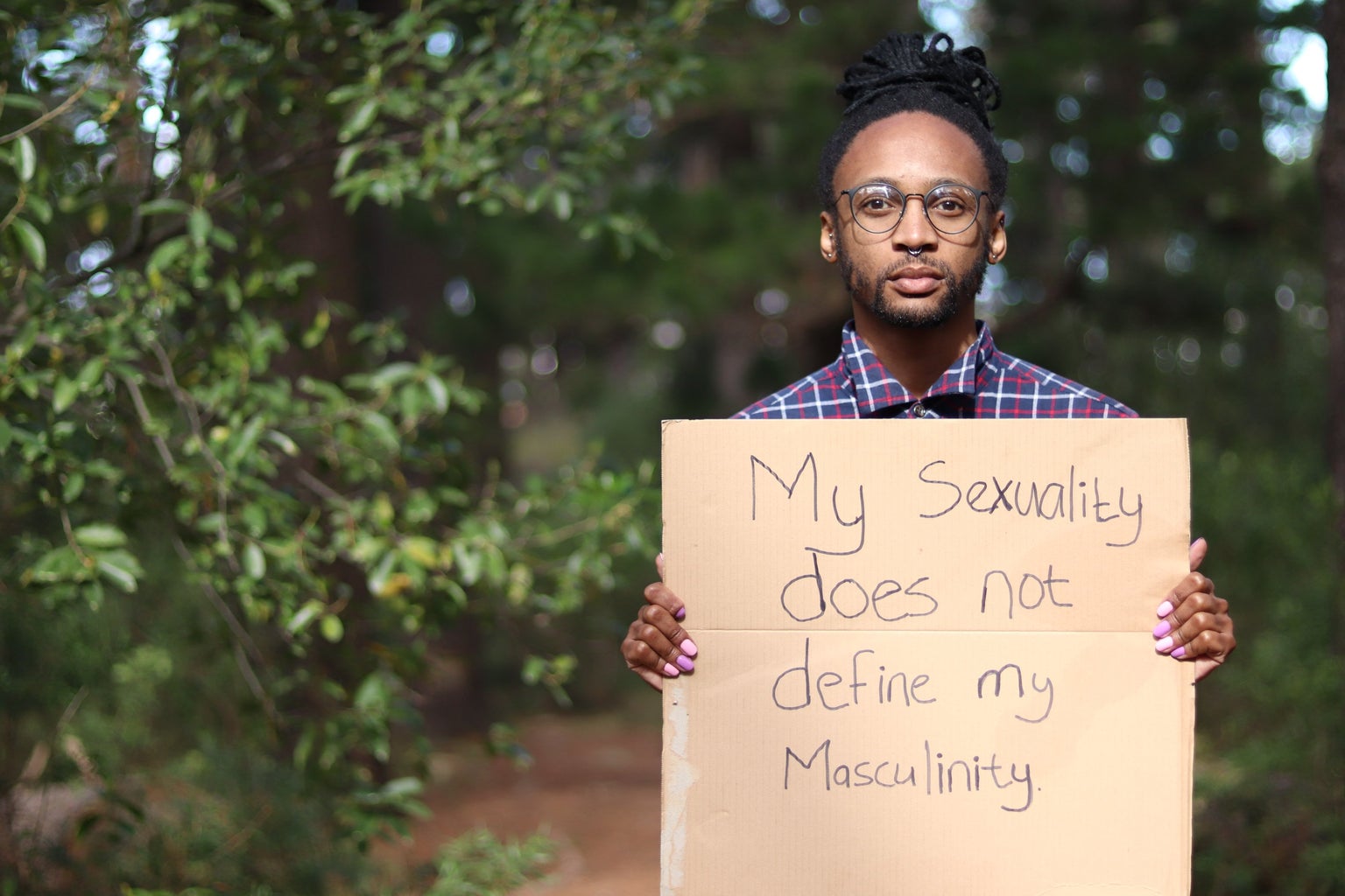 A Xhosa man holding a sign that says, \"My sexuality does not define my masculinity.\"