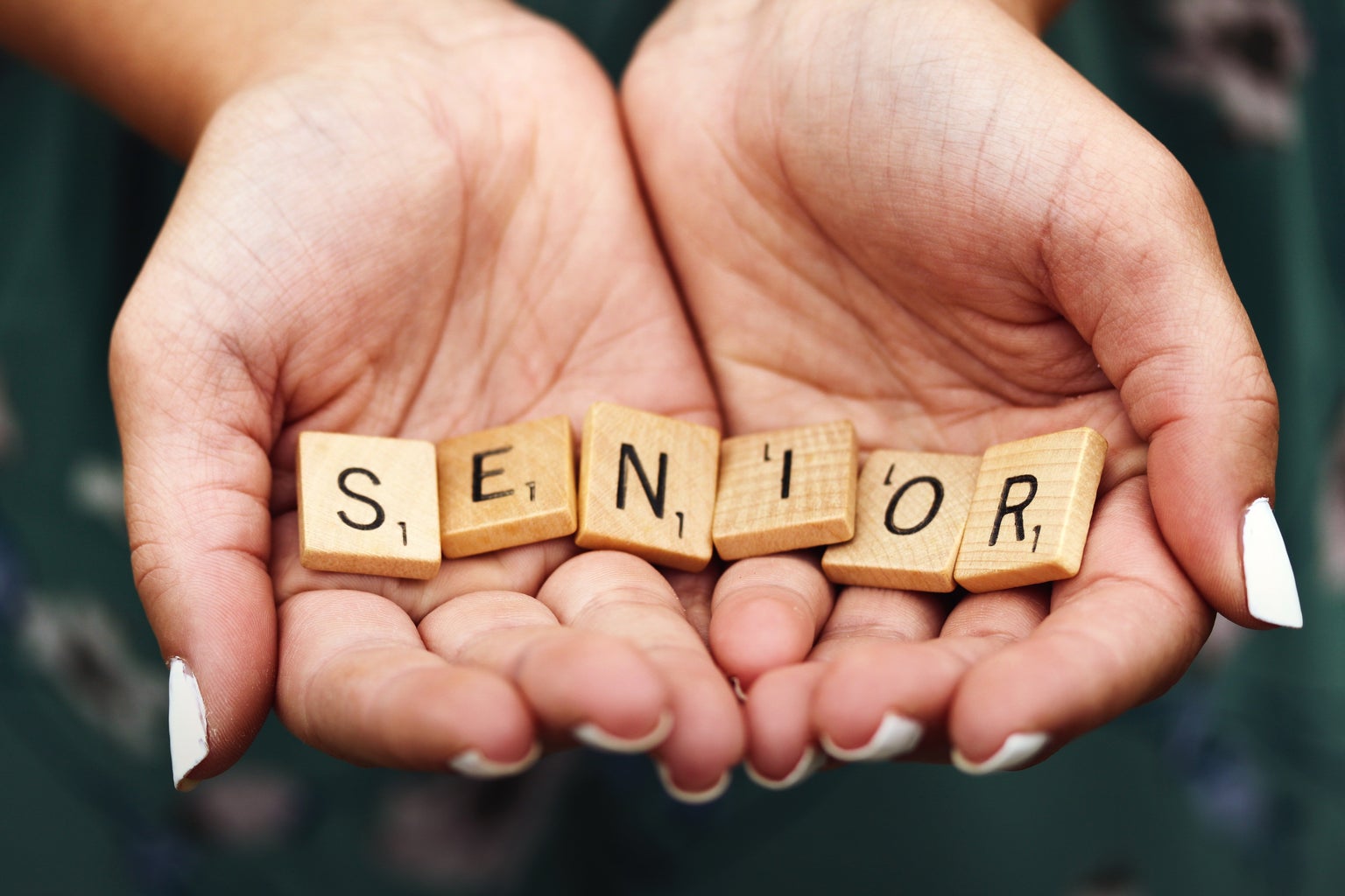 A girl with white nail polish holding scrabble letters spelling the word SENIOR
