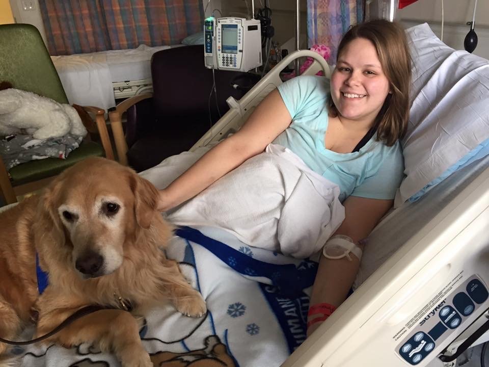 woman sitting in a hospital bed with a service dog