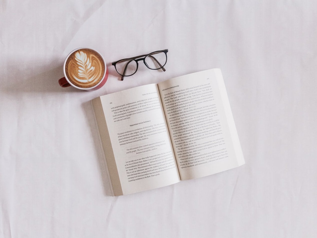 A pair of glasses, tea, and a book on a white surface