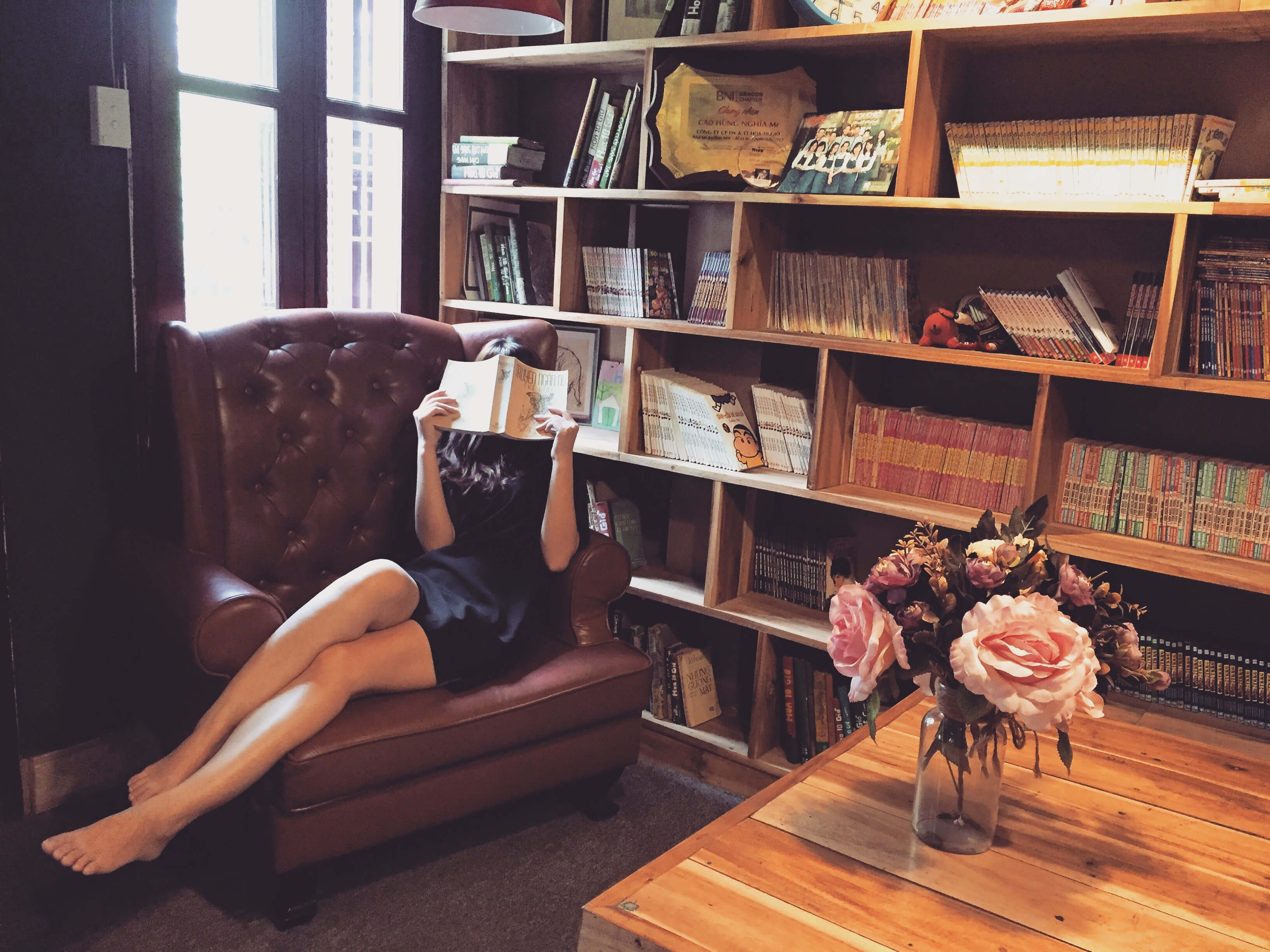 Woman hiding her face with a book in a library wearing a dress