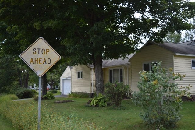 Faded sign that reads \"stop ahead\" in front of a small yellow cottage