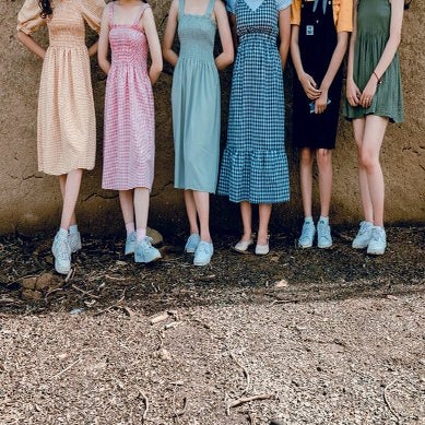 six women standing in dresses against a cliff