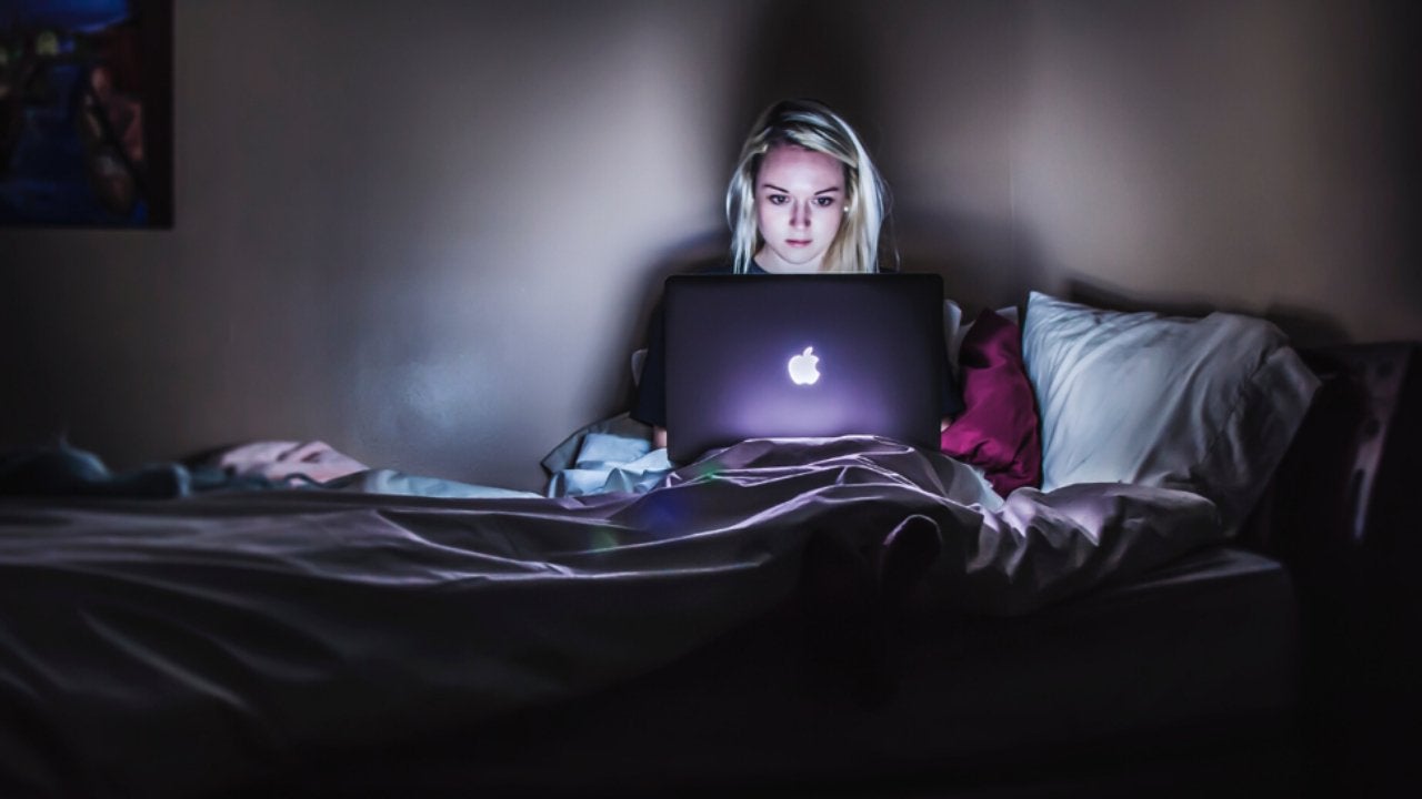 woman sitting on bed with MacBook on lap