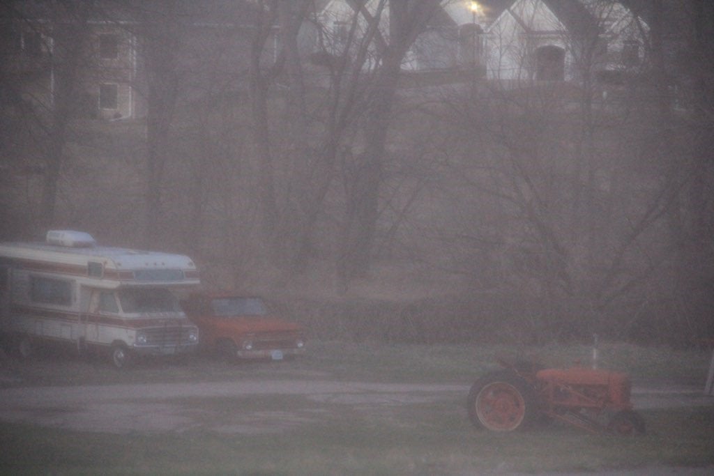 An old tractor and Rv in a farmhouse\'s front yard.