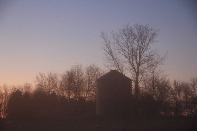 Silhouette of a farm at sunset.
