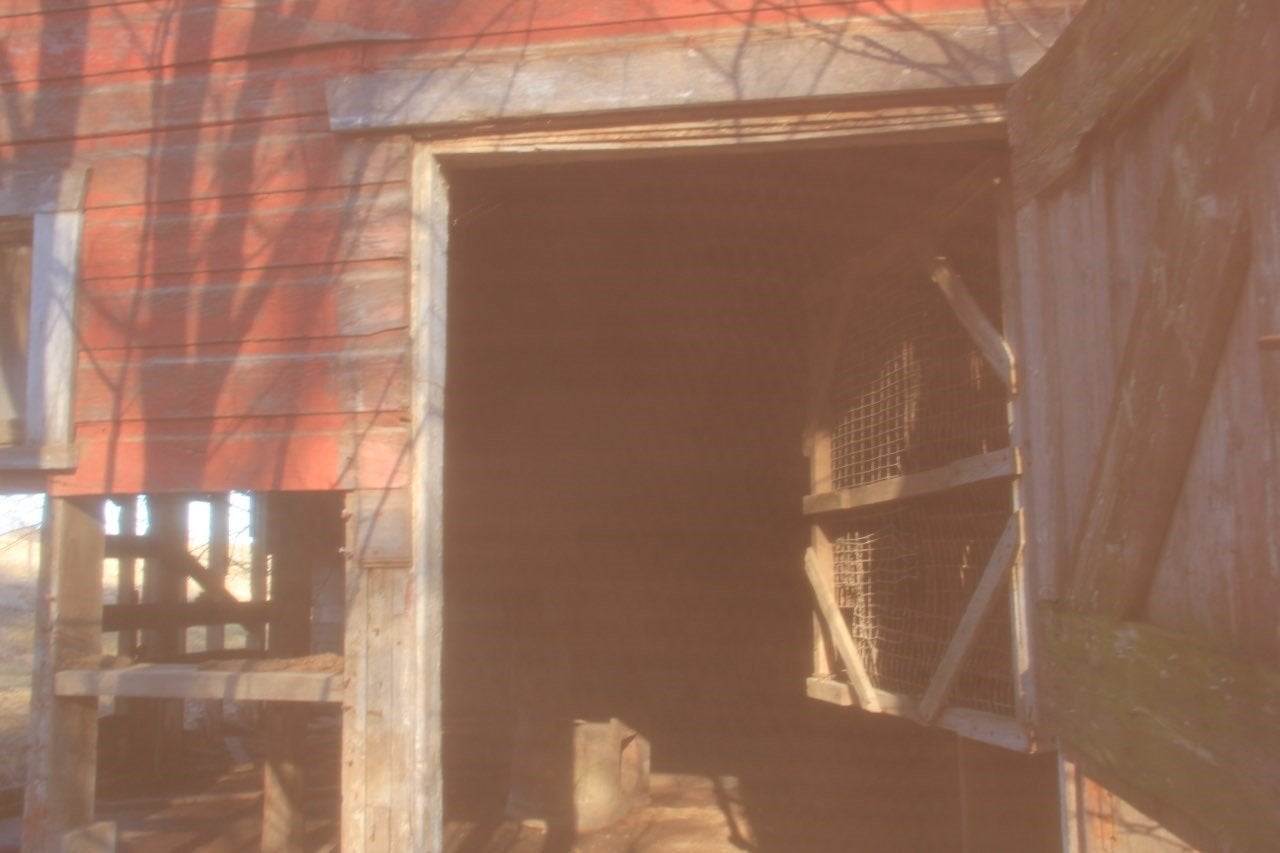 A doorway to an abandoned, red barn, bathed in natural sunlight.