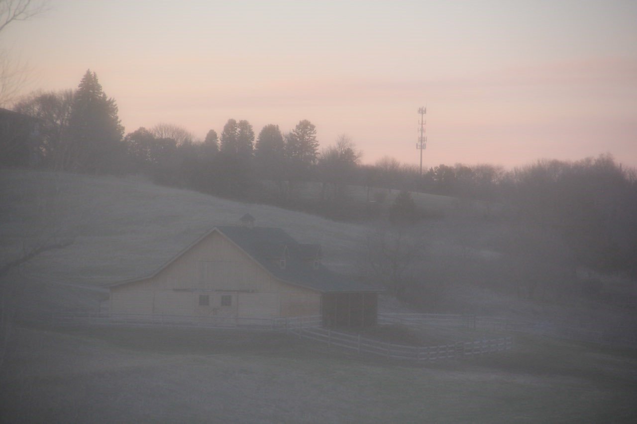 A wooden barn built into the hills in sunlight.