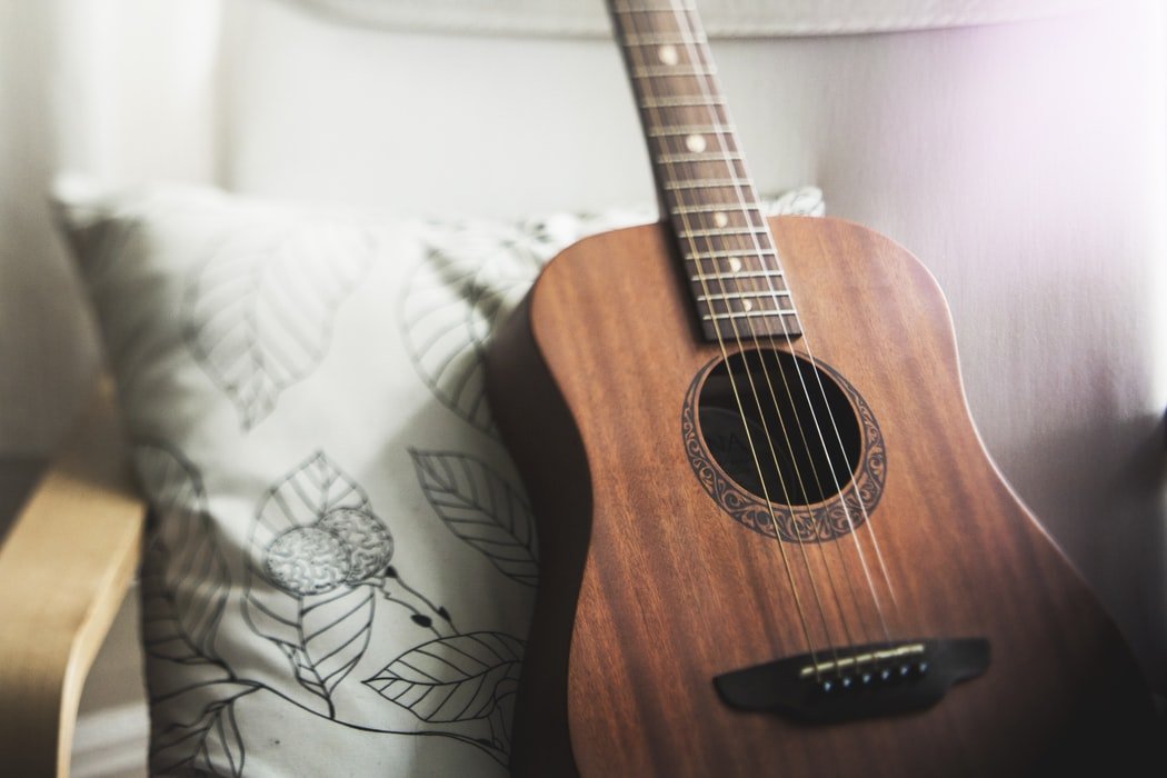 A brown guitar sitting on a white chair with a pillow.