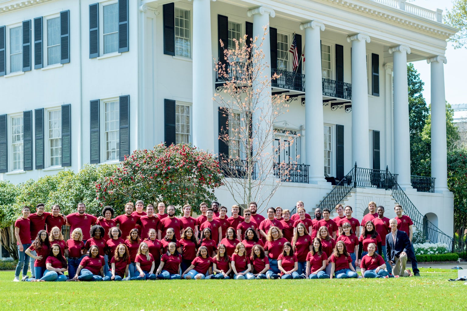 People in garnet shirts posing in front of a white building