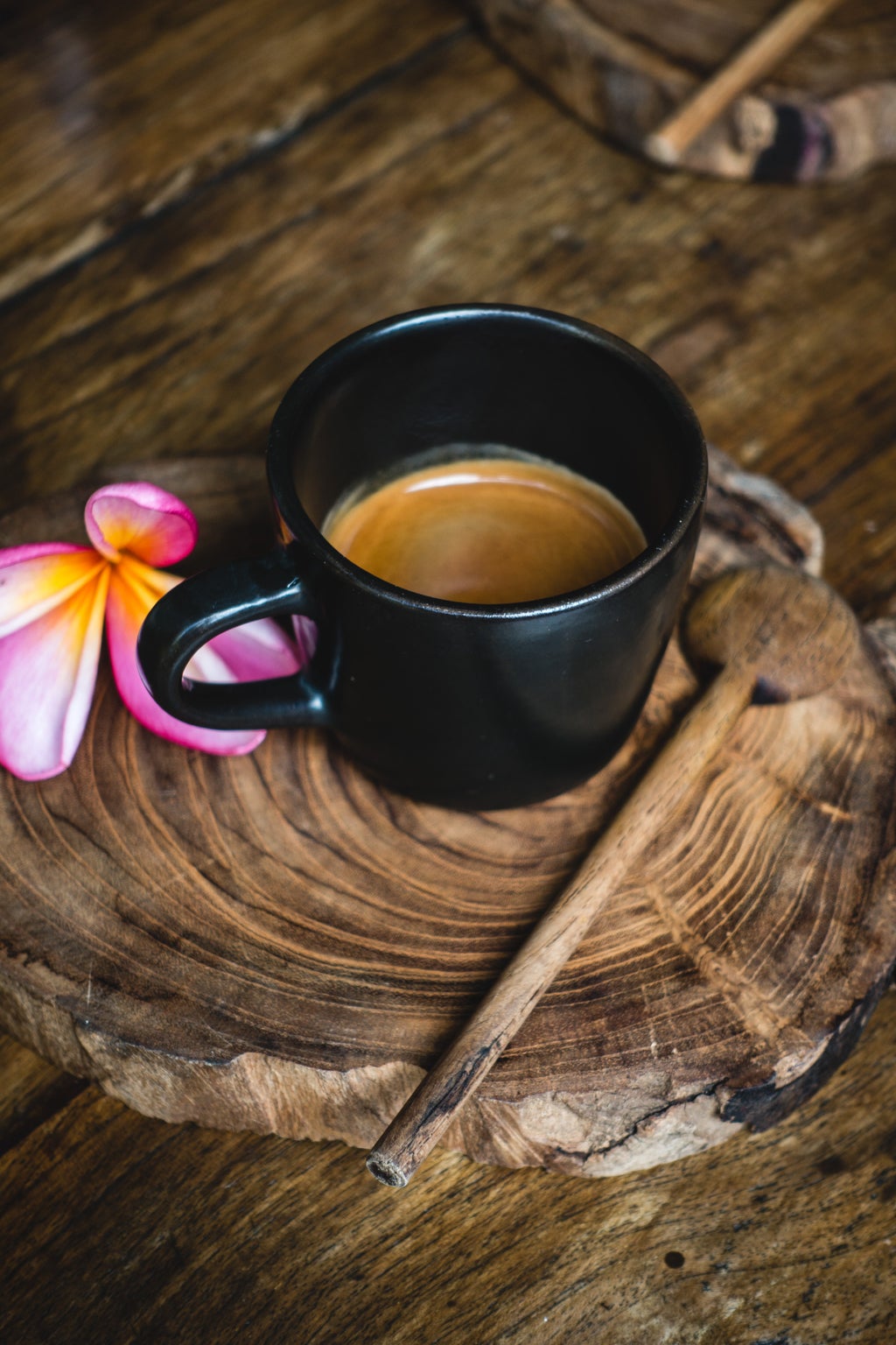 coffee in a black mug with a pink flower next to it