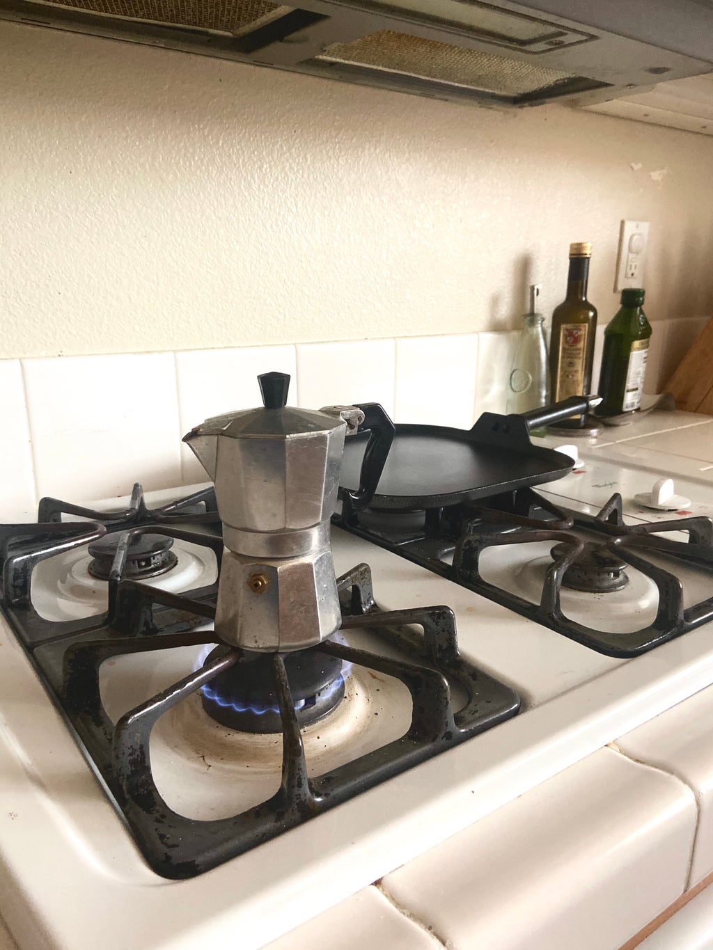 coffee maker over a stove top with a pan in the back drop