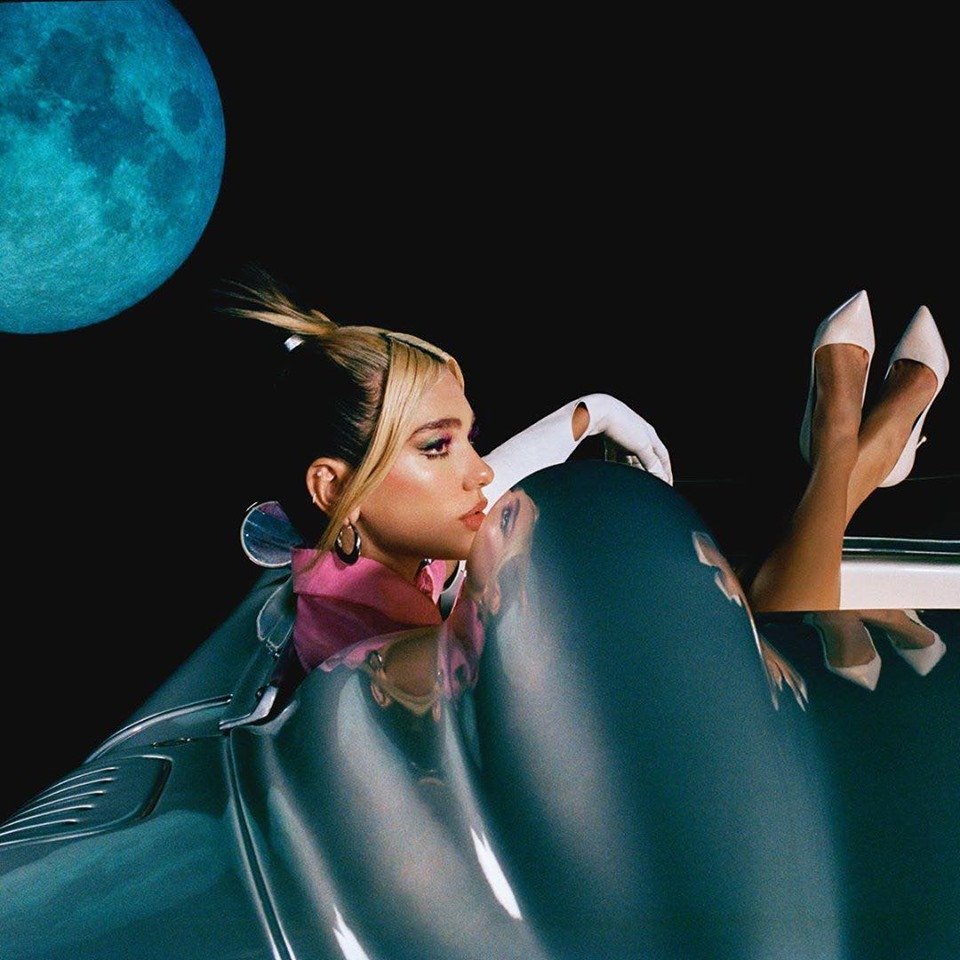 Side shot of Dua Lipa with her feet up in a convertible car