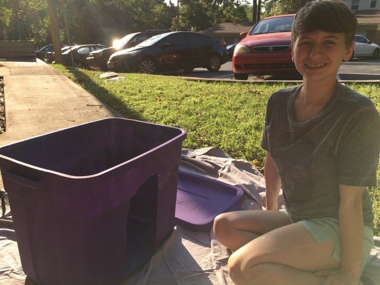 Lindsey sits outside while painting a storage container