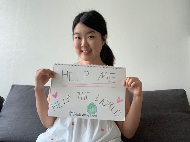 girl holding a hand drawn sign that reads \"help me help the world\" with an illustration of earth