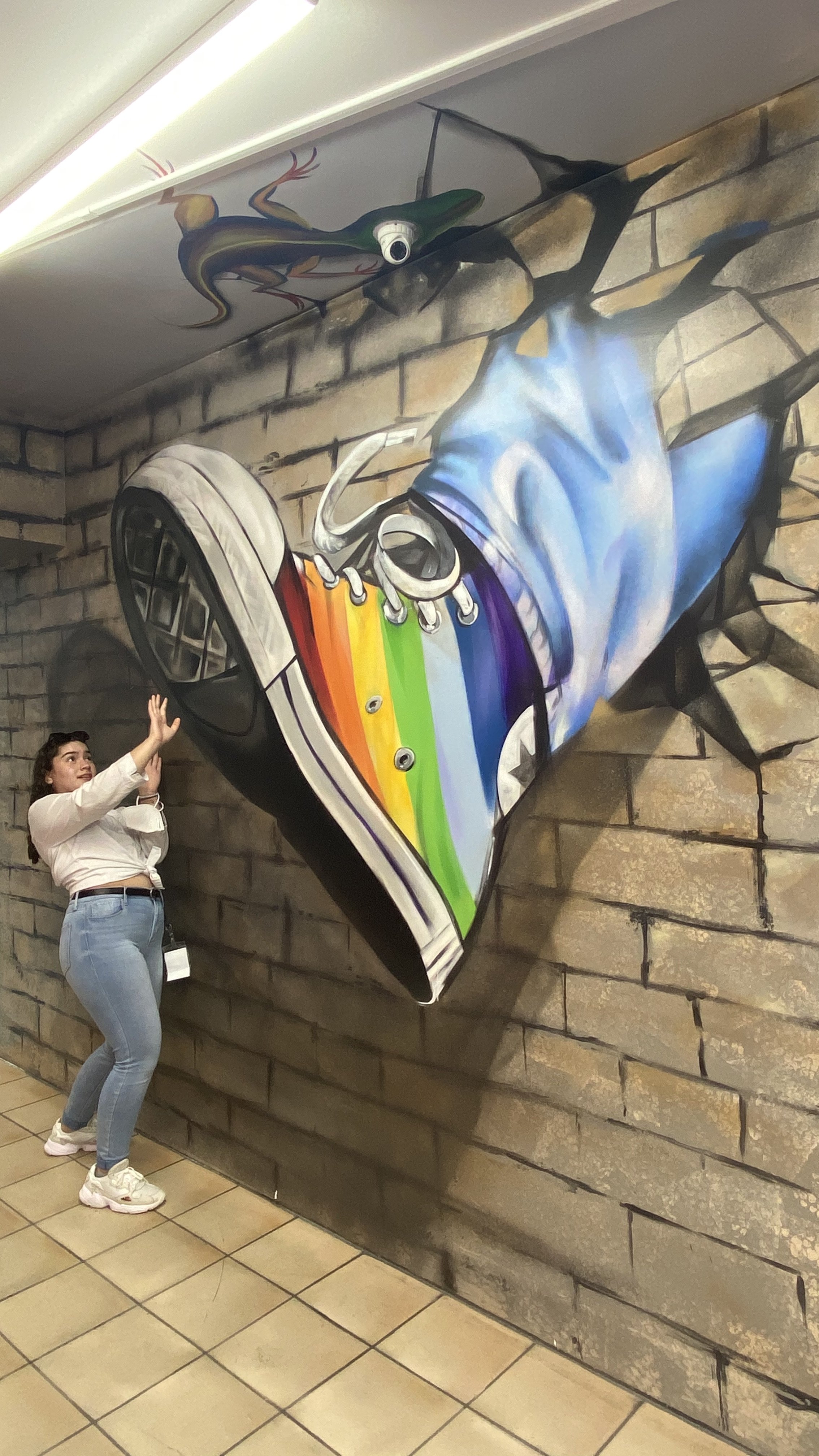 Girl posing with a art wall illusion of a colorful shoe.