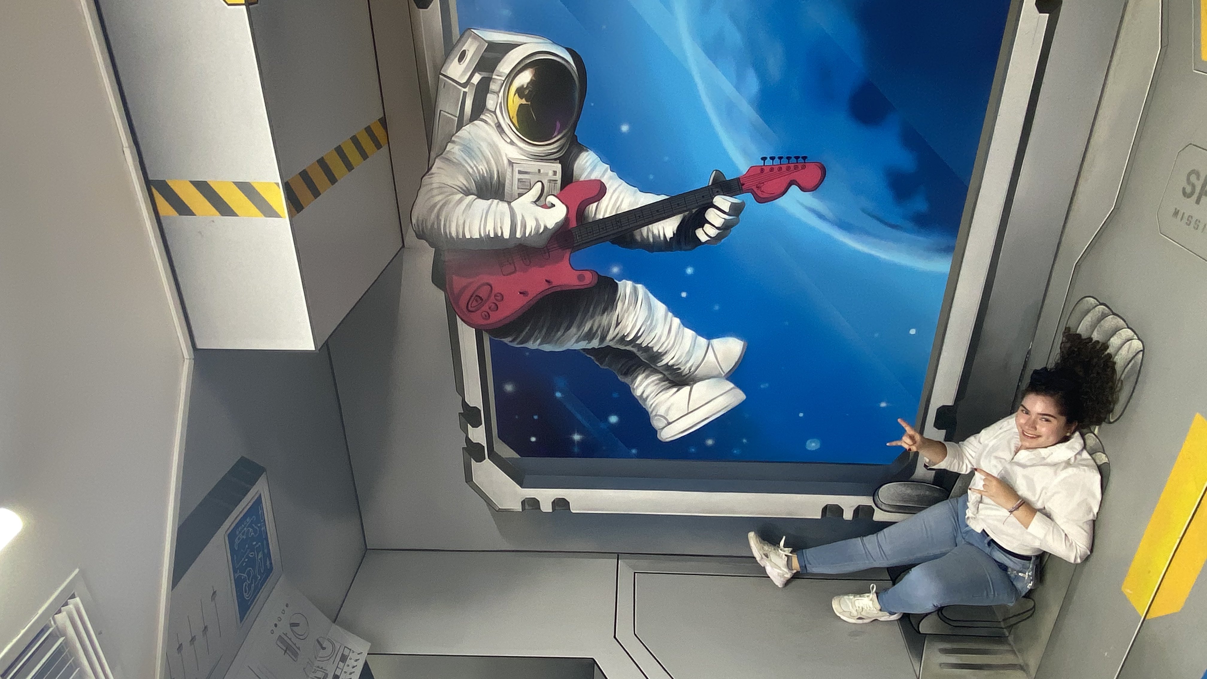Girl posing with an art wall illusion of an astronaut in space