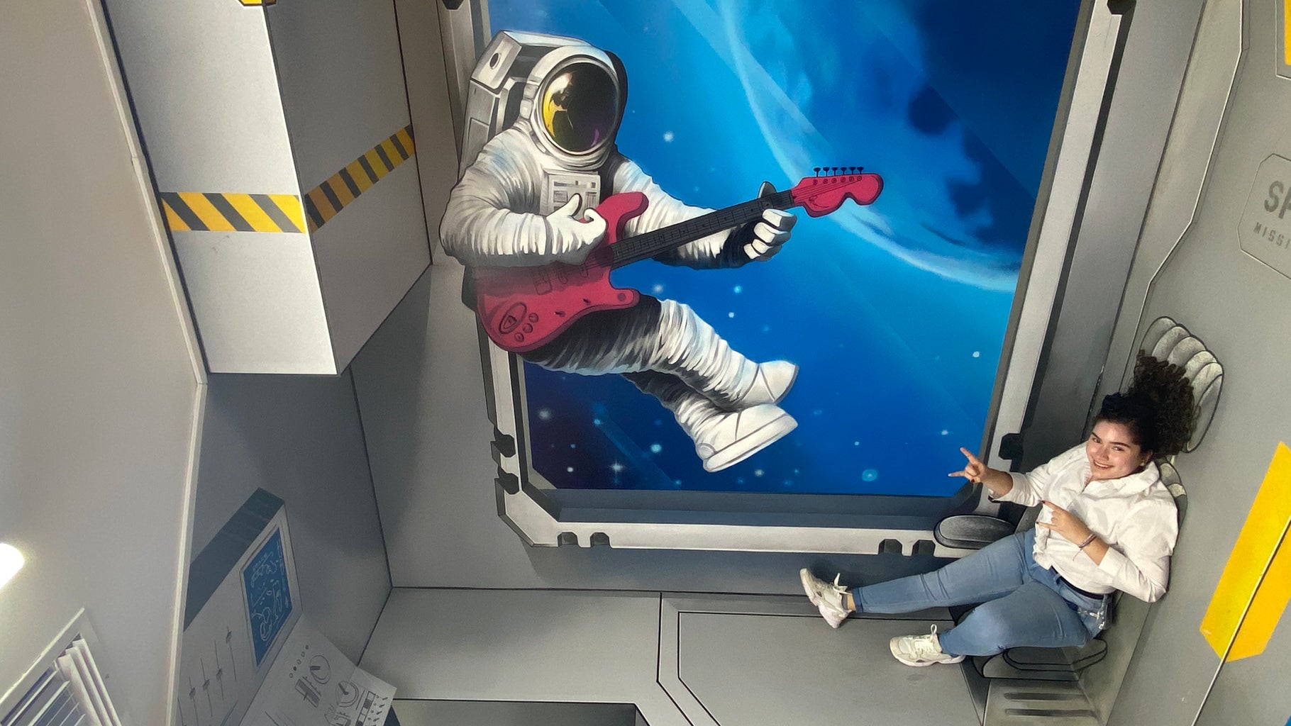 Girl posing with an art wall illusion of an astronaut in space