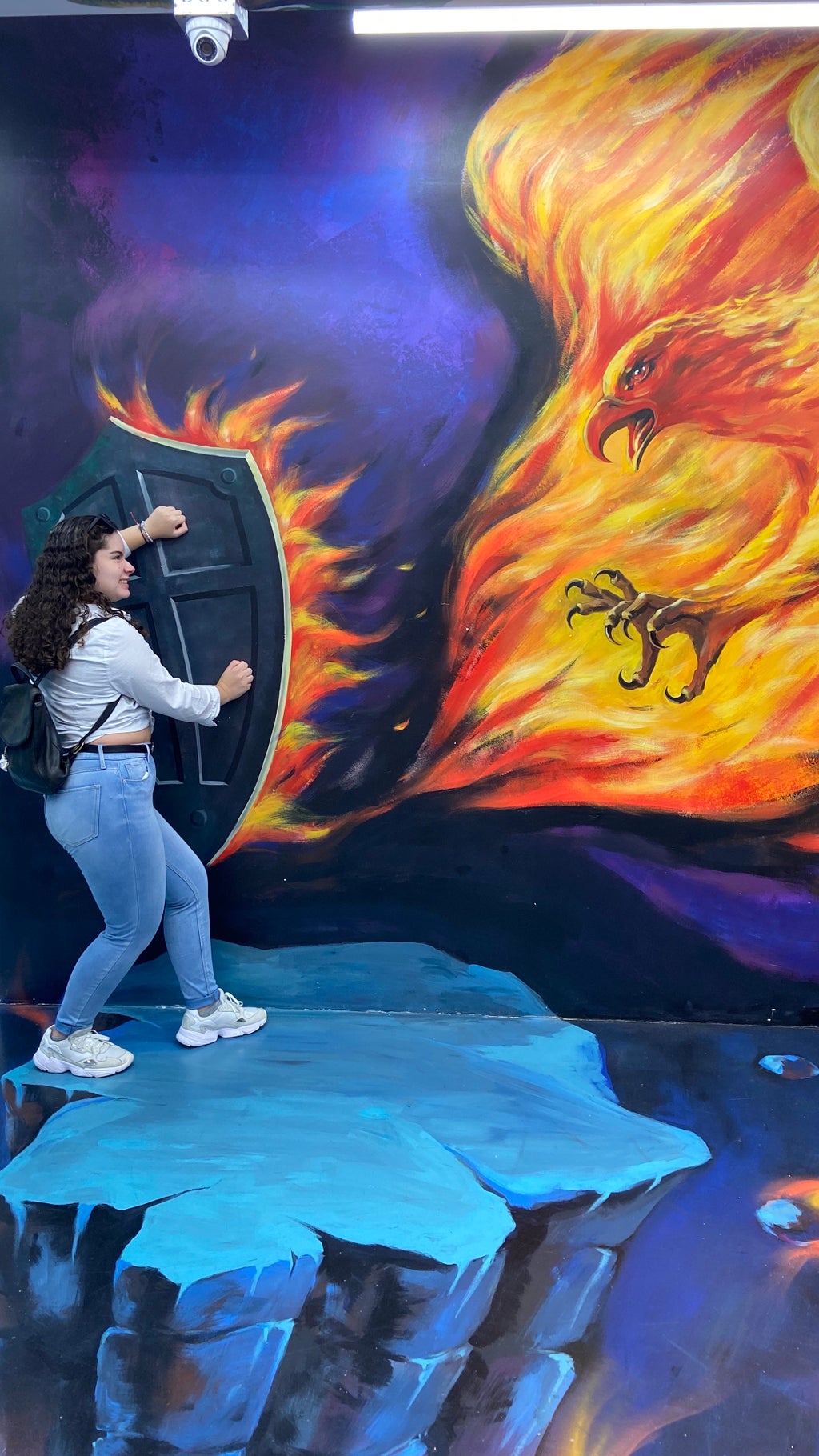 Girl posing with art wall illusion of a firebird and a shield
