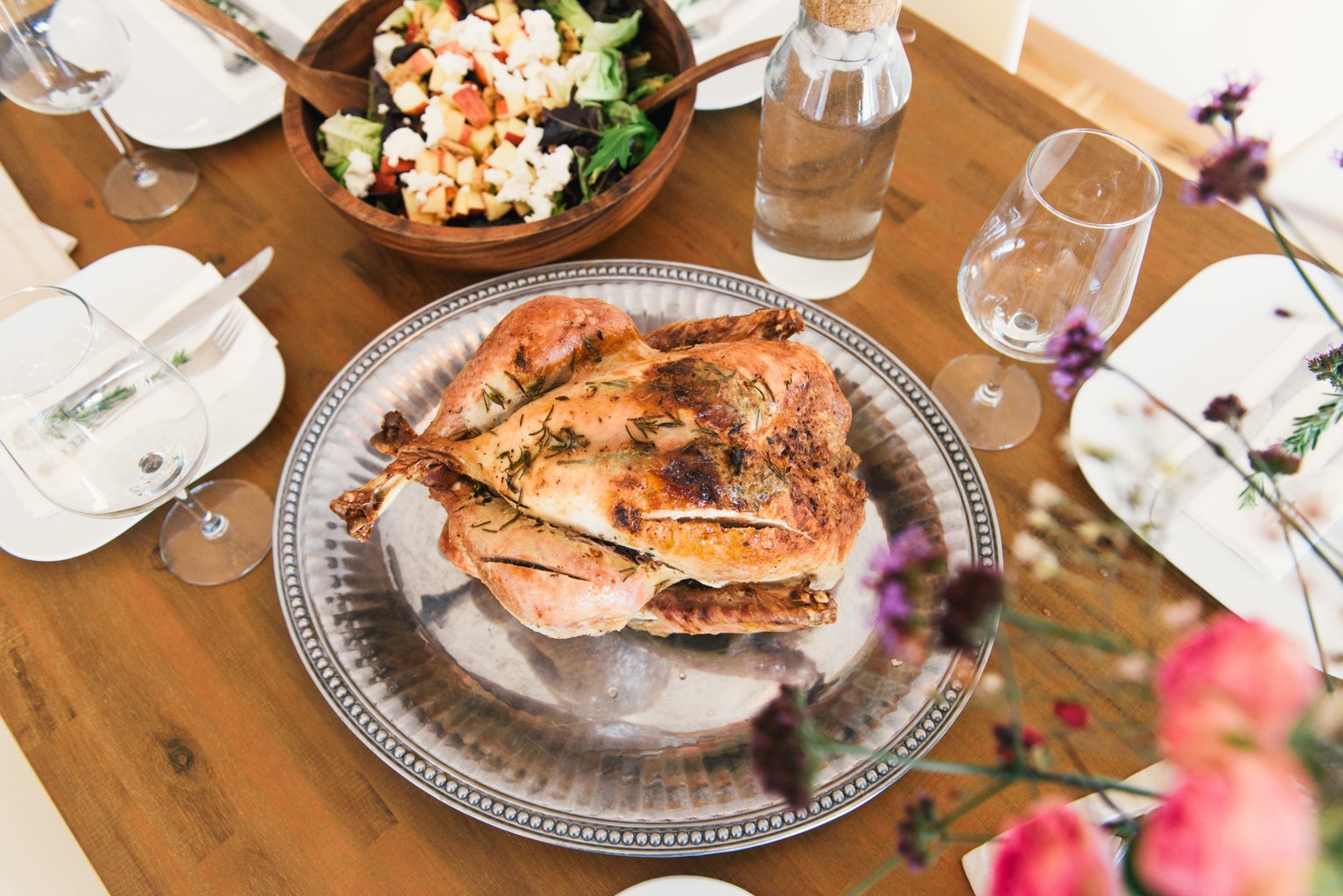 roasted chicken on a wooden table with sides and place settings