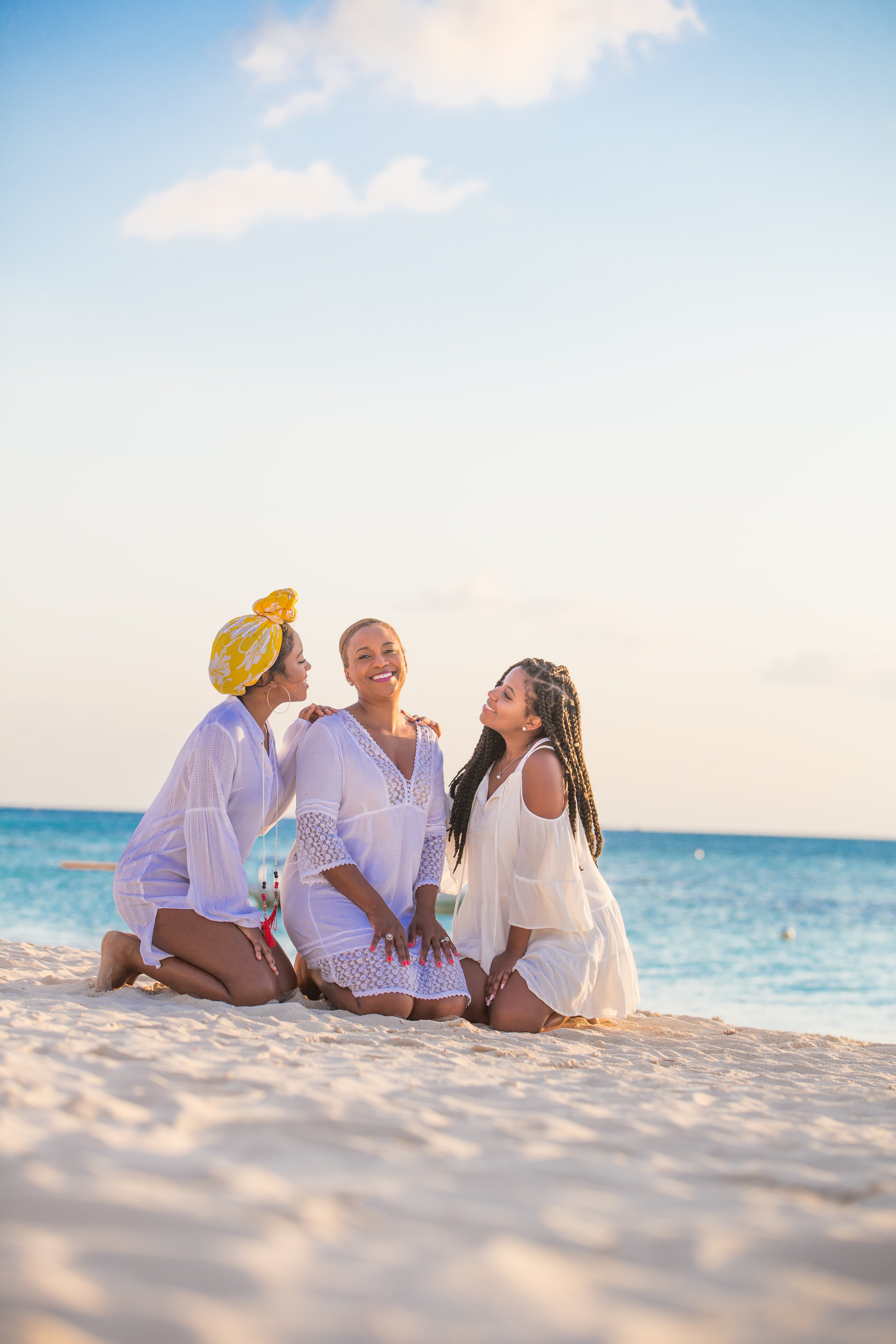 woman in white dress sitting on beach during daytime next two other women in blue dresses