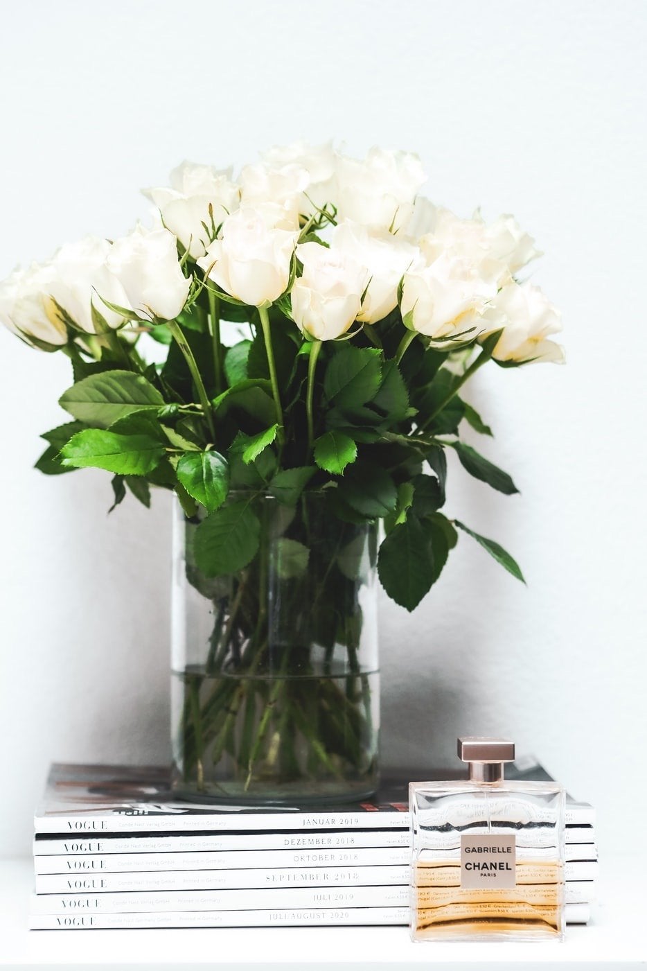 white tabletop with vase of white roses and two books, a bottle of Chanel perfume