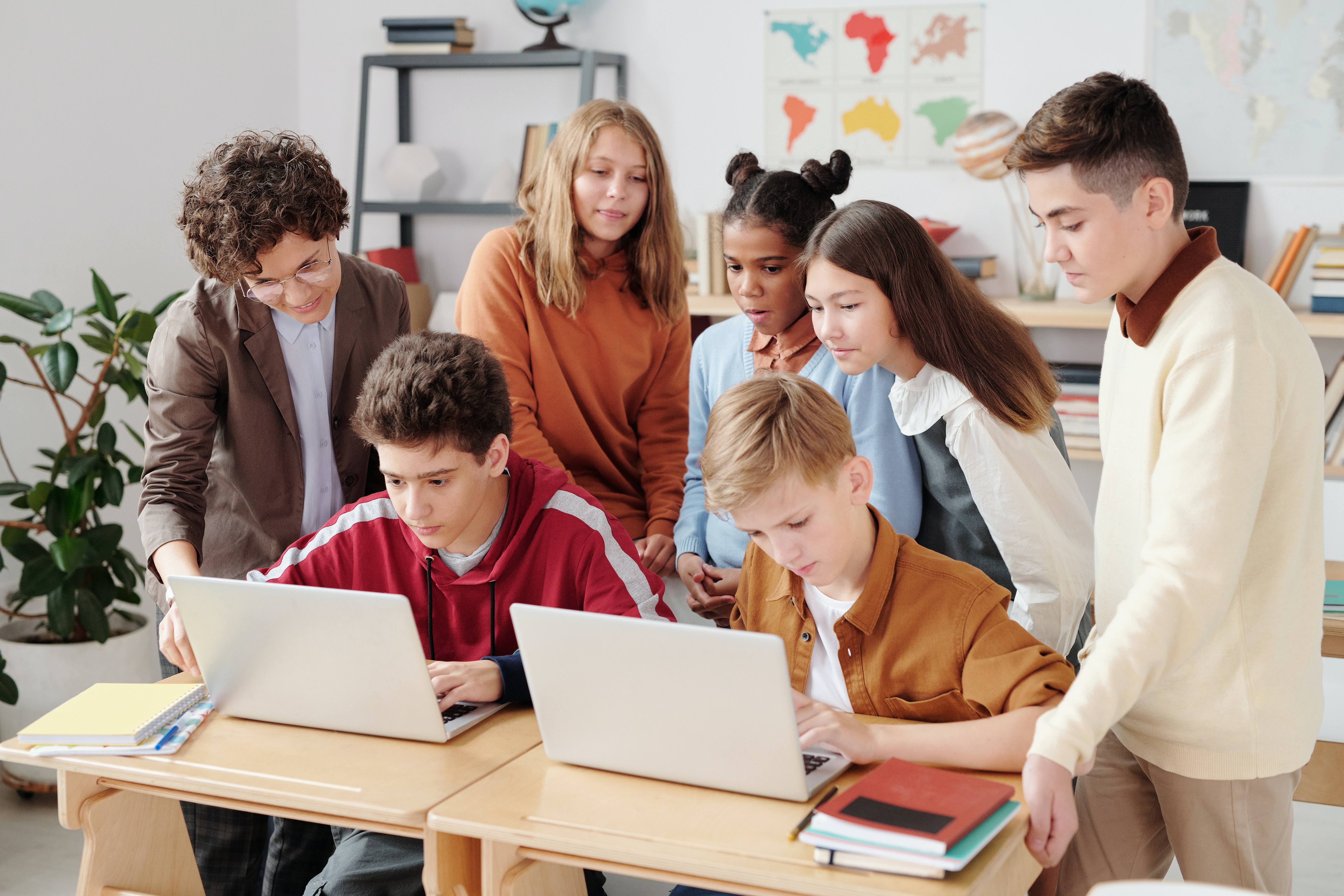 A group of kids in a classroom gather together to look at laptops .
