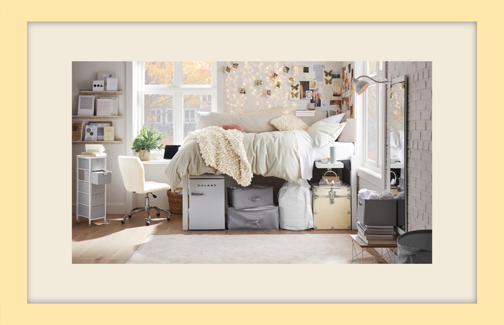 Dorm room with a bed, fairy lights, pictures, storage, and a desk chair.