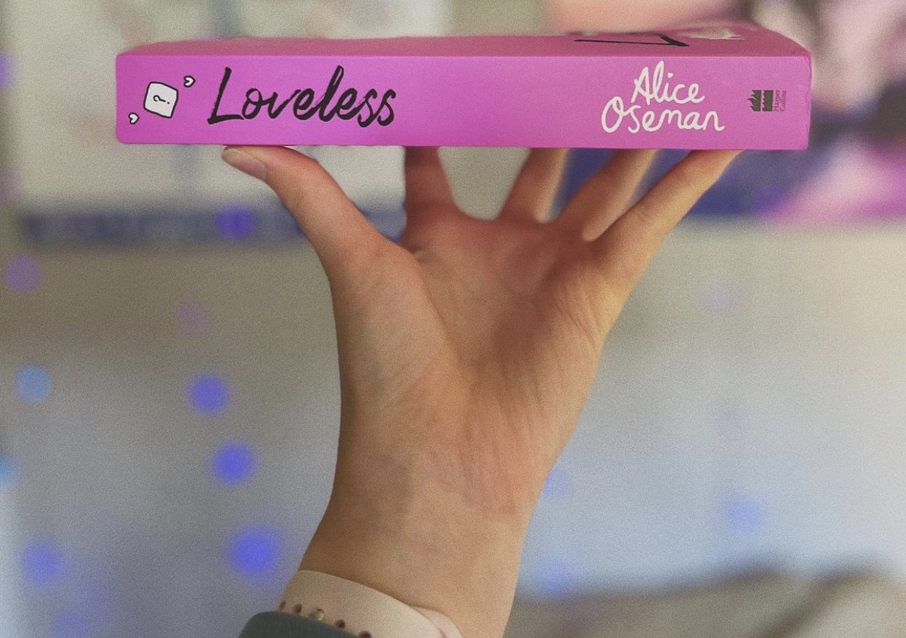 A hand holding a copy of Loveless by Alice Oseman.