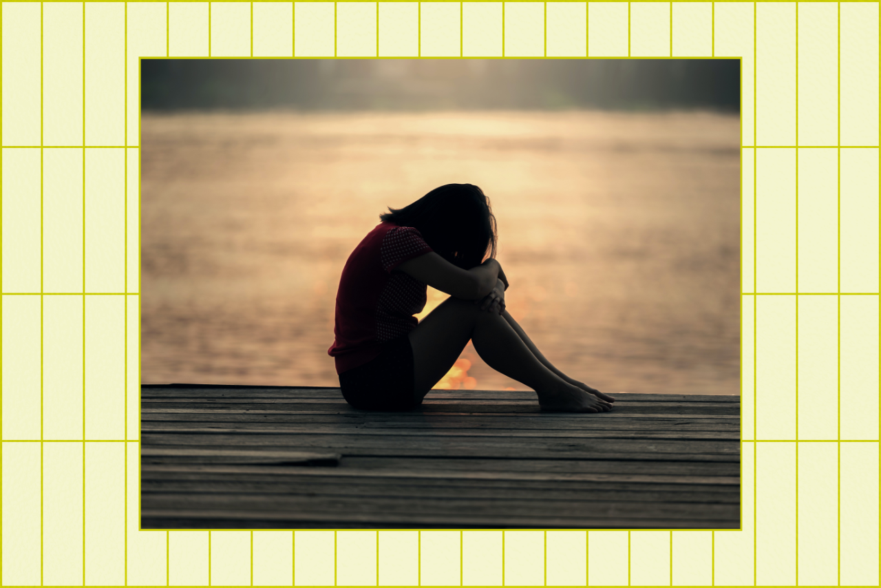 Woman sitting sadly by water.