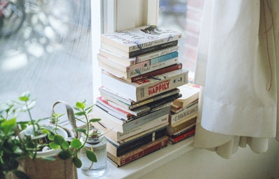 a stack of books on a window sill, next to a plant