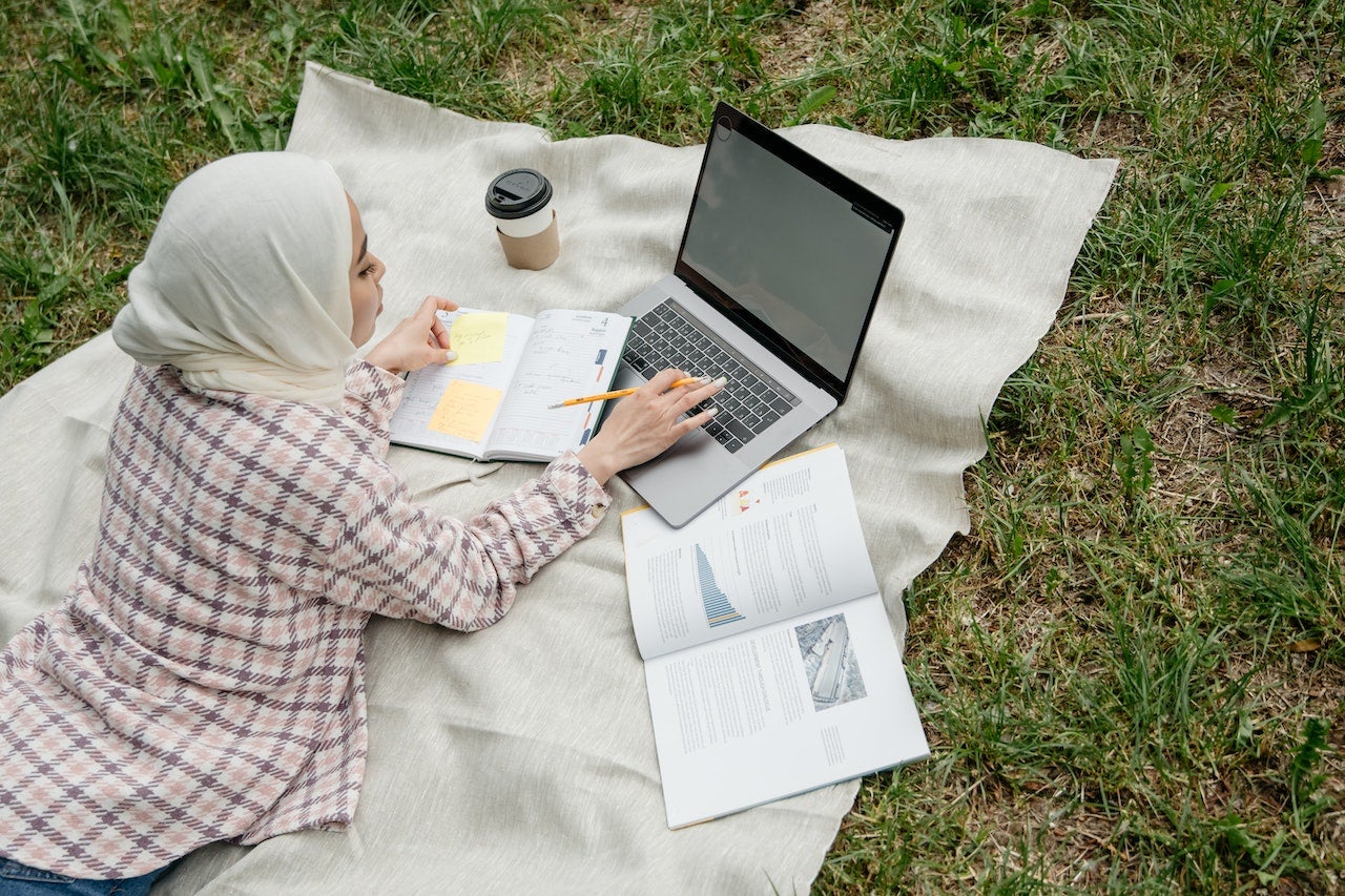 women in hijab studying on picnic blanket