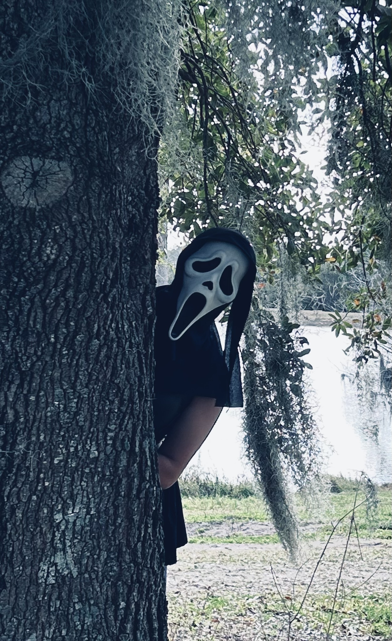 Girl with ghostface mask looking around a tree