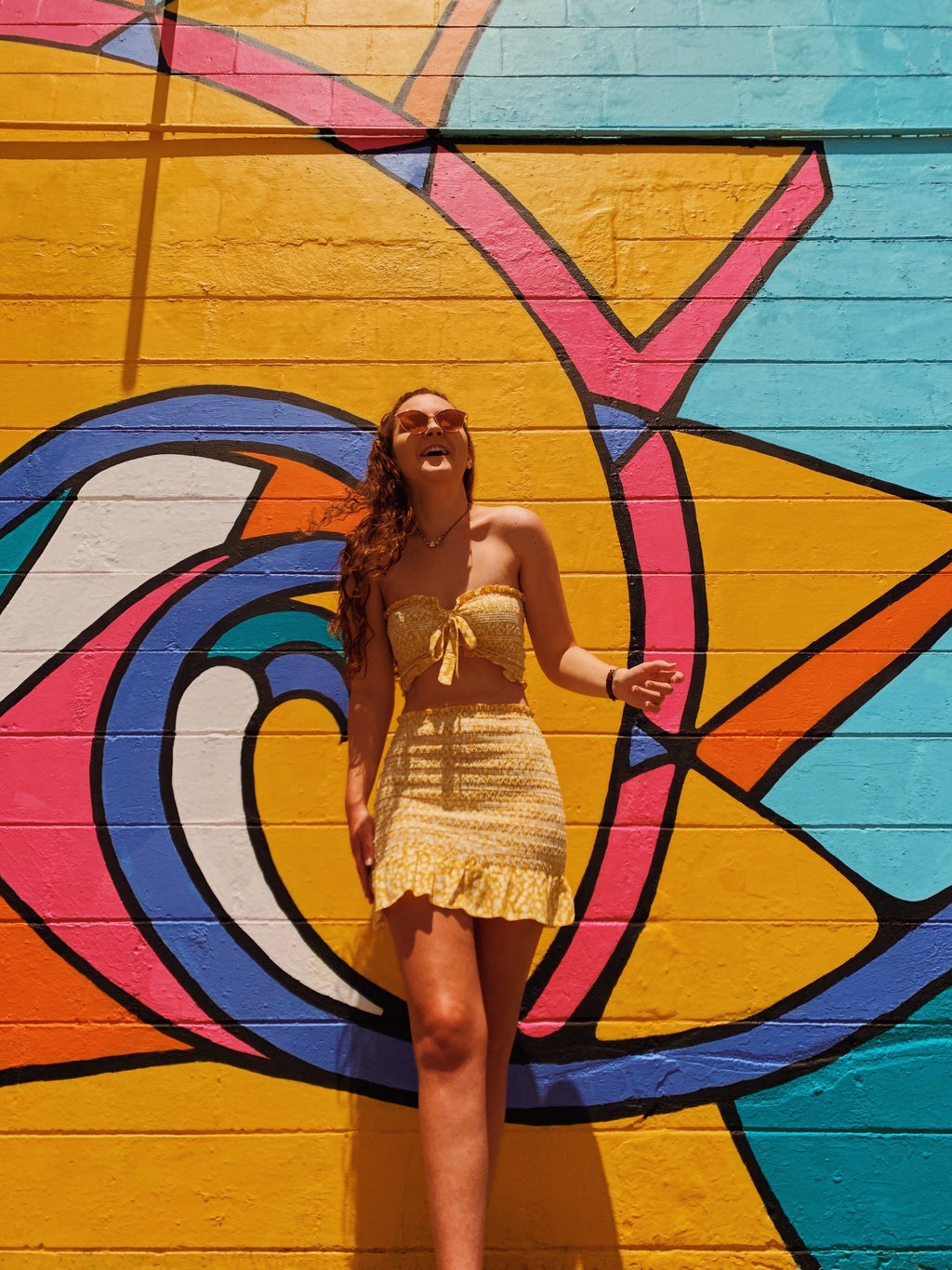 Becca McCandless wearing yellow dress in front of colorful sun wall
