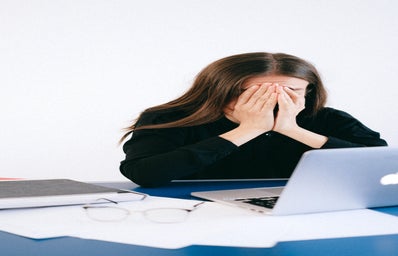 stressed person covering face sitting at laptop