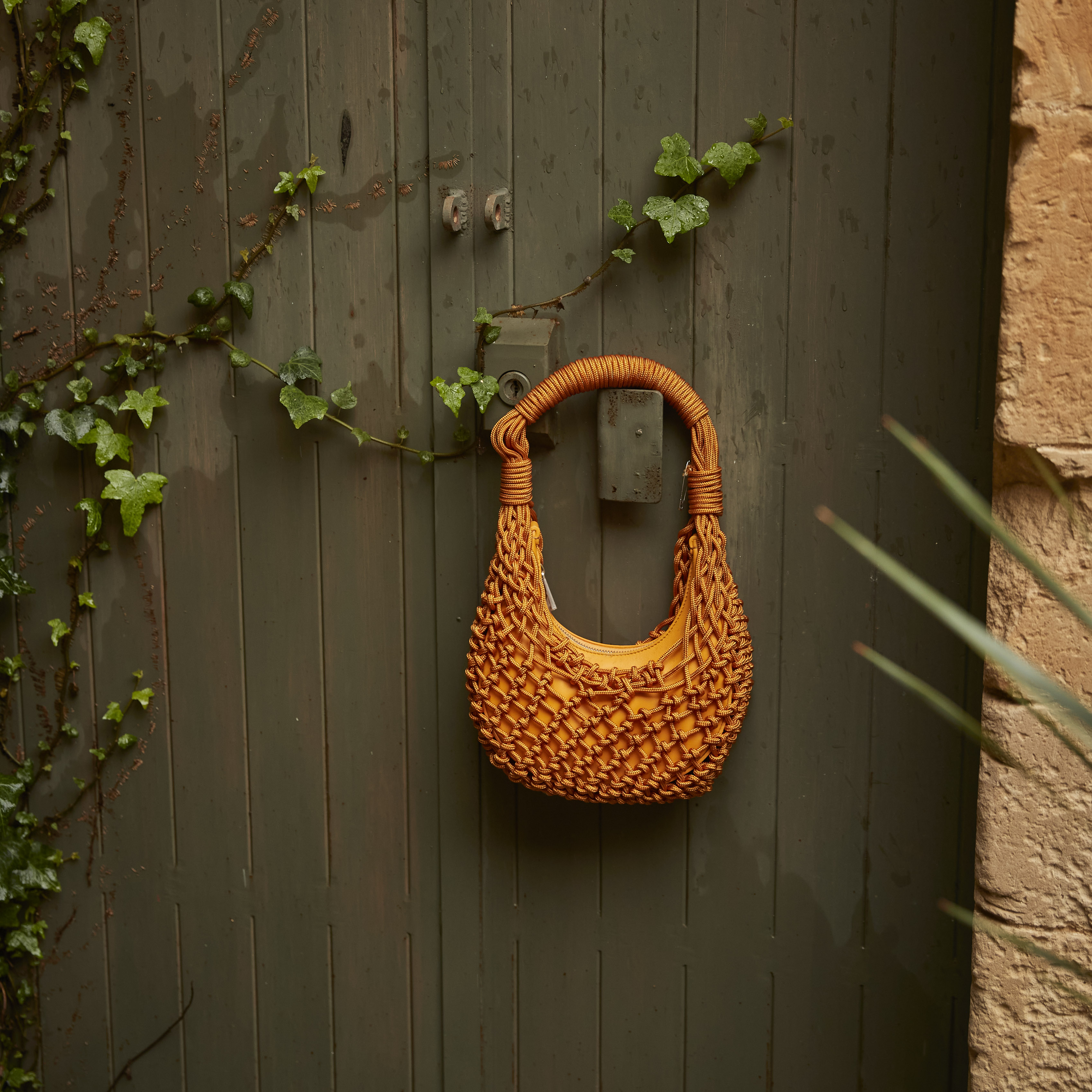 Orange woven purse hanging on a door next to a vine