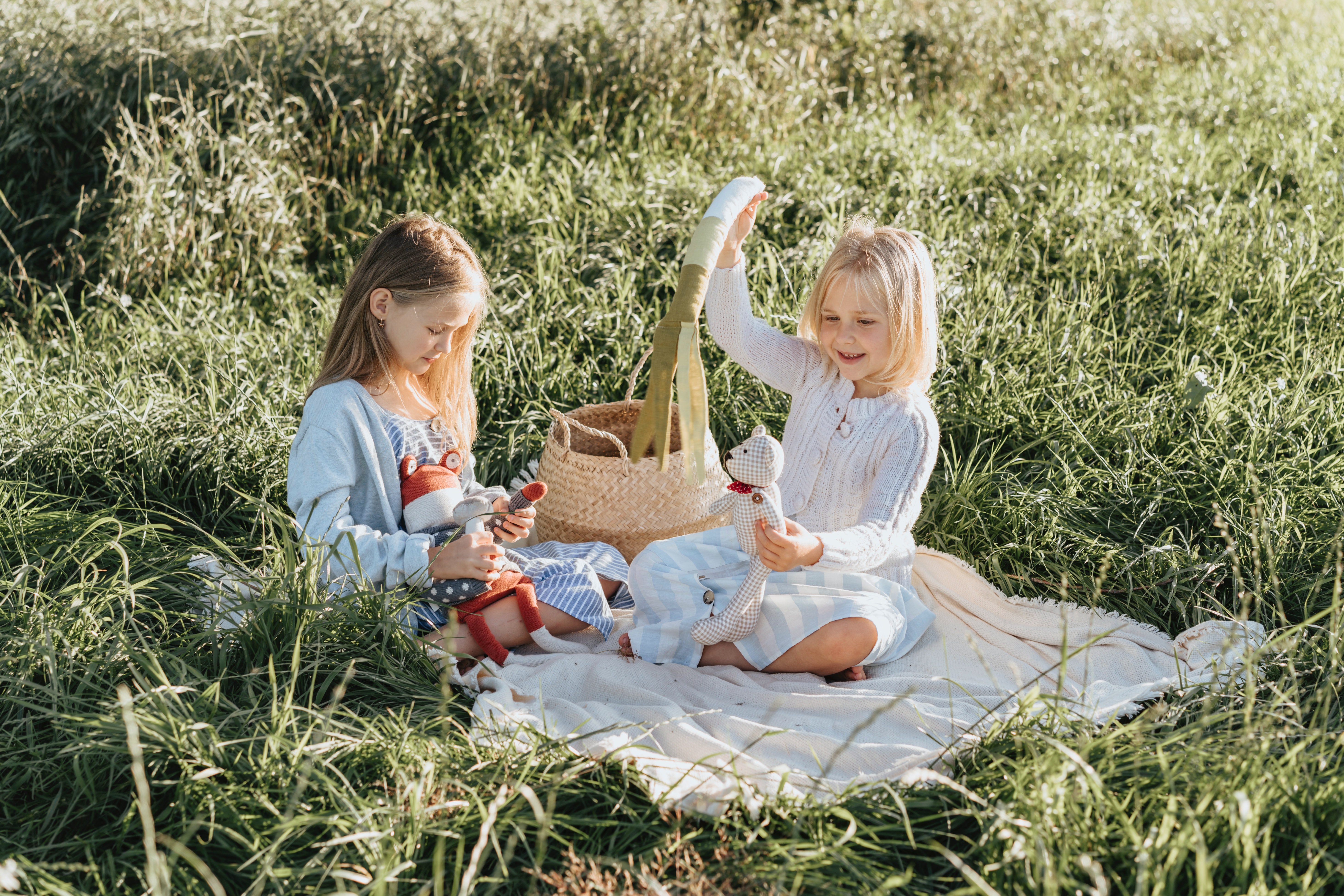 Two girls playing with dolls on a picnic blanket