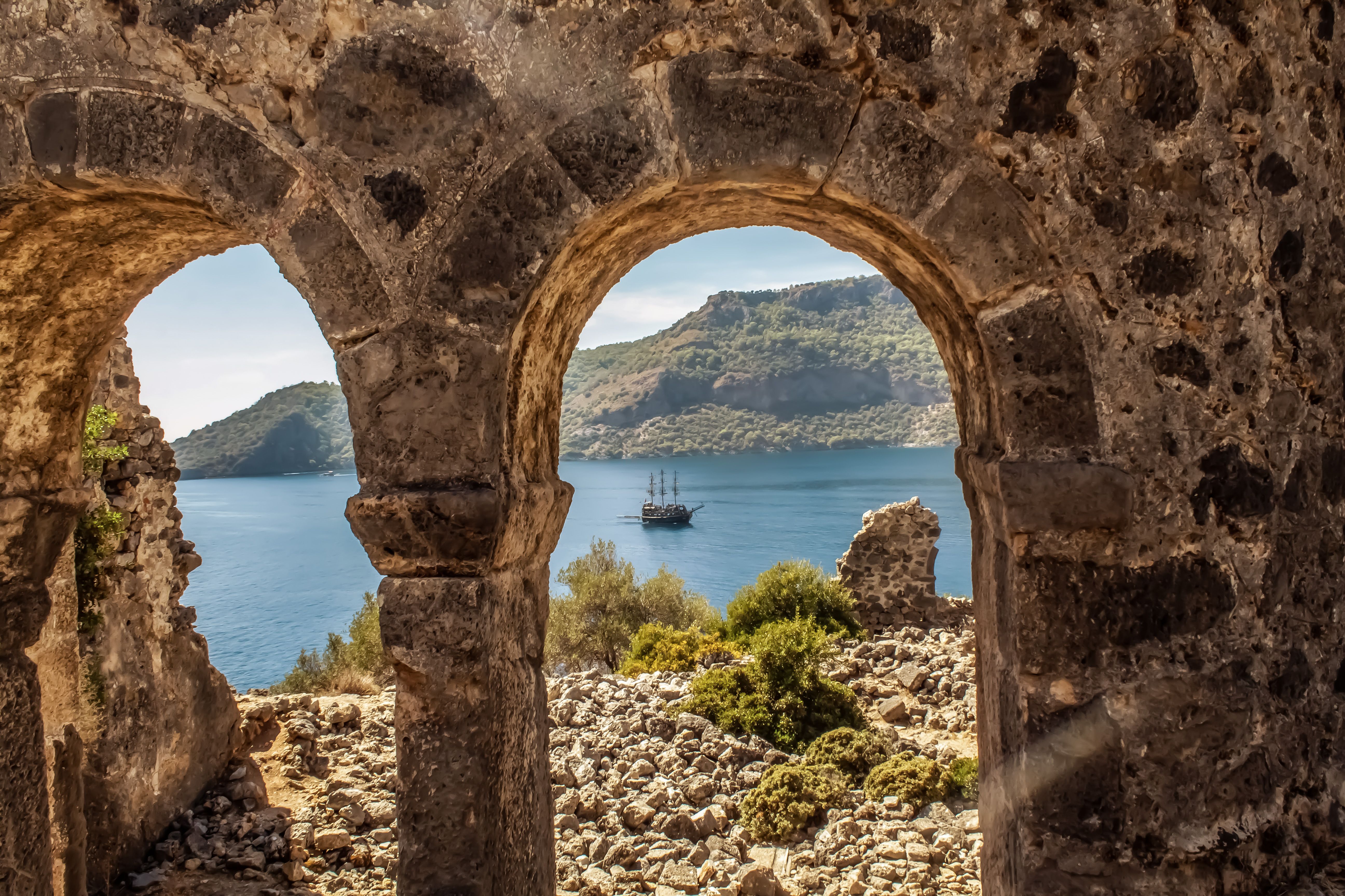A stone arch with a boat and mountains in the background