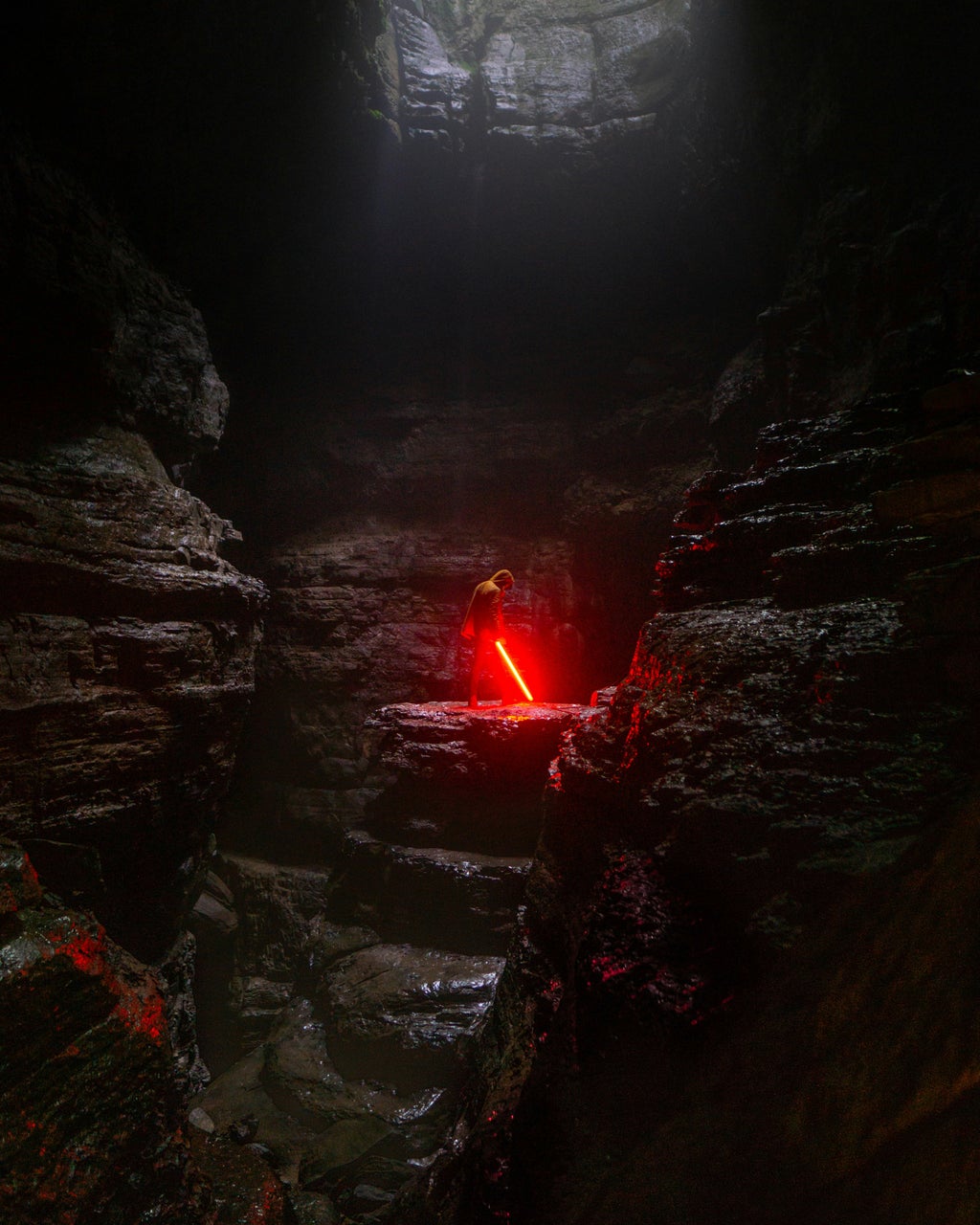 A lone figure stands in the middle of a cave holding a red lightsaber.