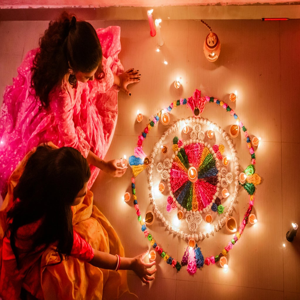 Women Sitting on the Floor Holding Candles Beside Colorful Flowers During Diwali Festival