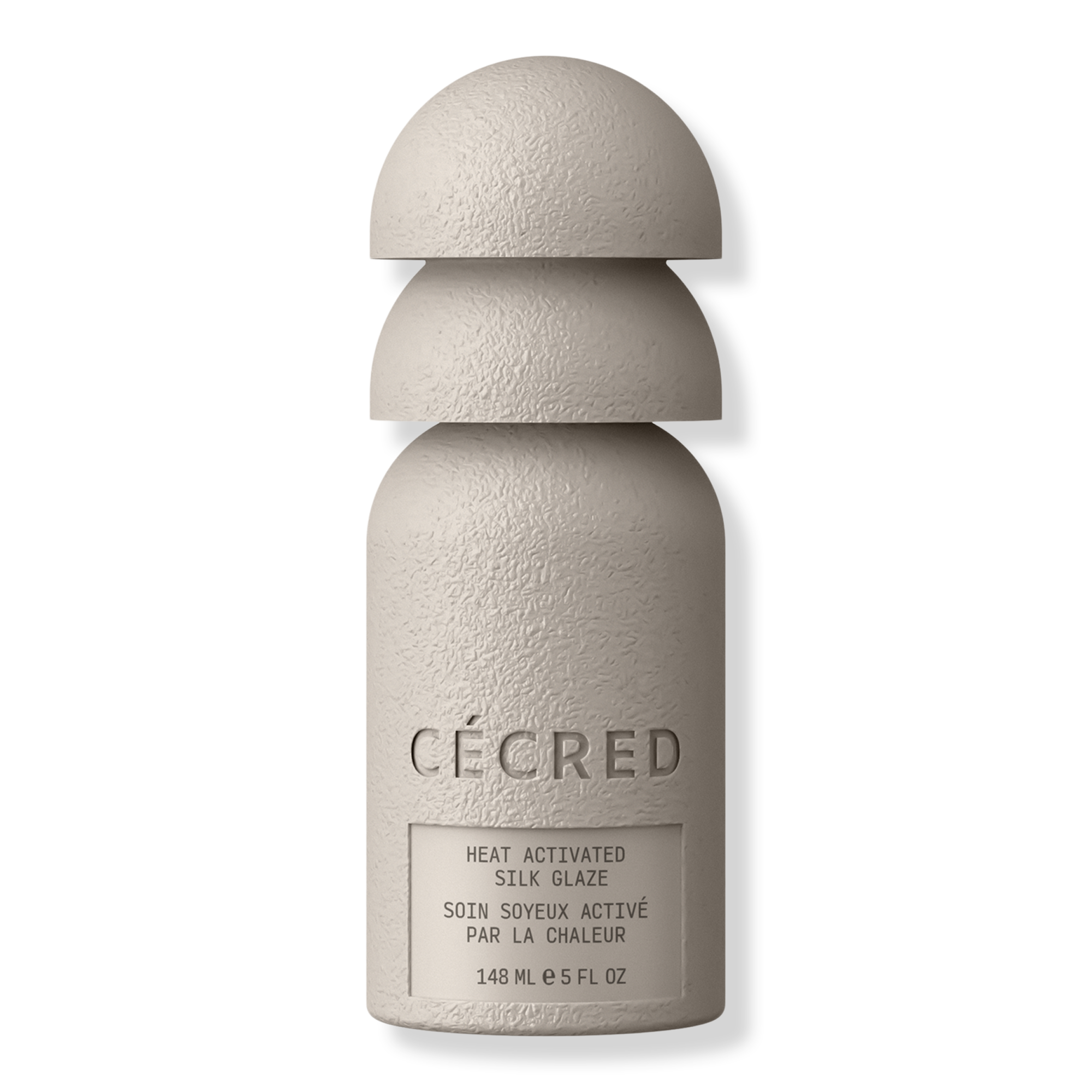 A textured white bottle of Cécred heat-activated silk glaze stands against a black background, its sculptural stacked cap creating a sleek, minimalist feel.