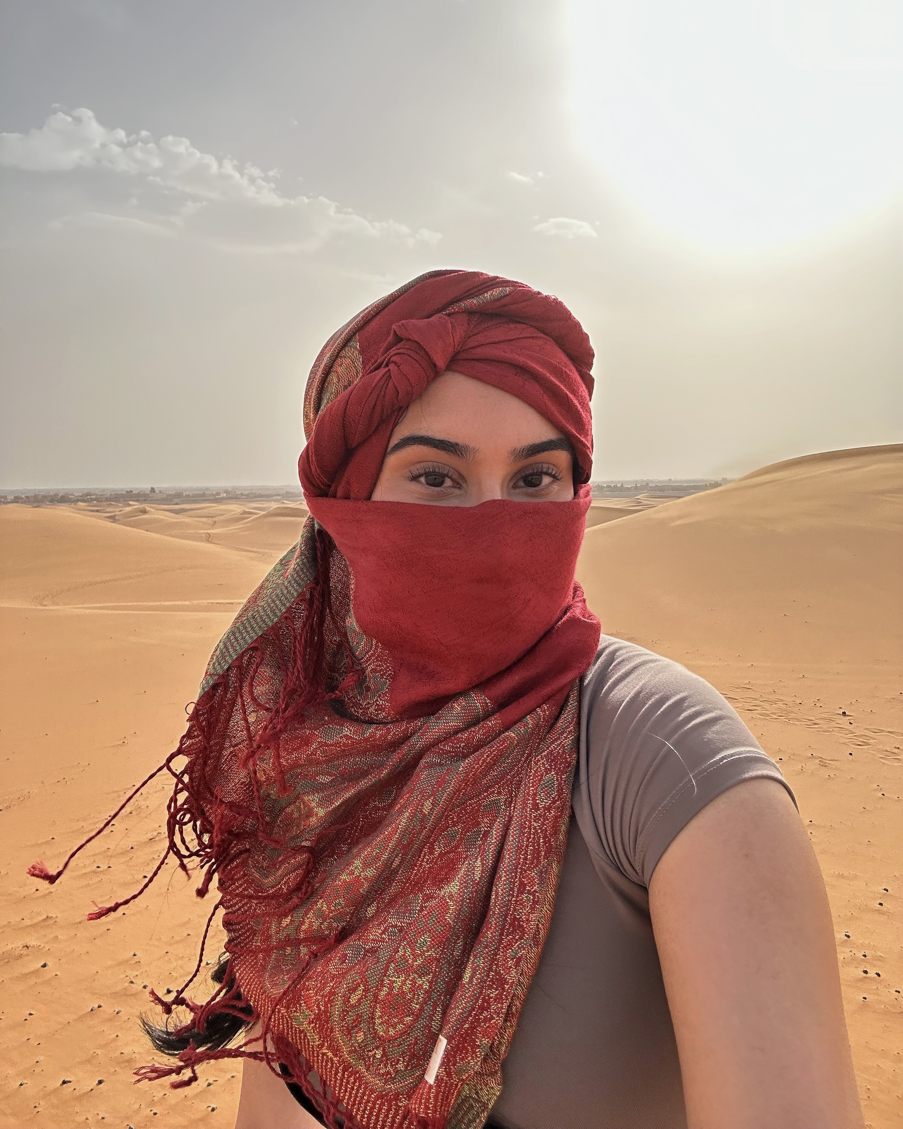 Woman in the Sahara Desert wearing a red scarf wrapped around her nose and mouth to shield from sandy winds.