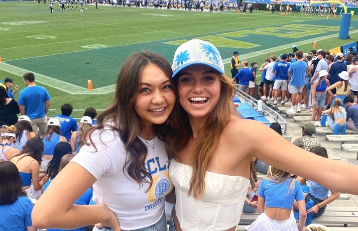 Two girls stand in UCLA merch at a UCLA football game.