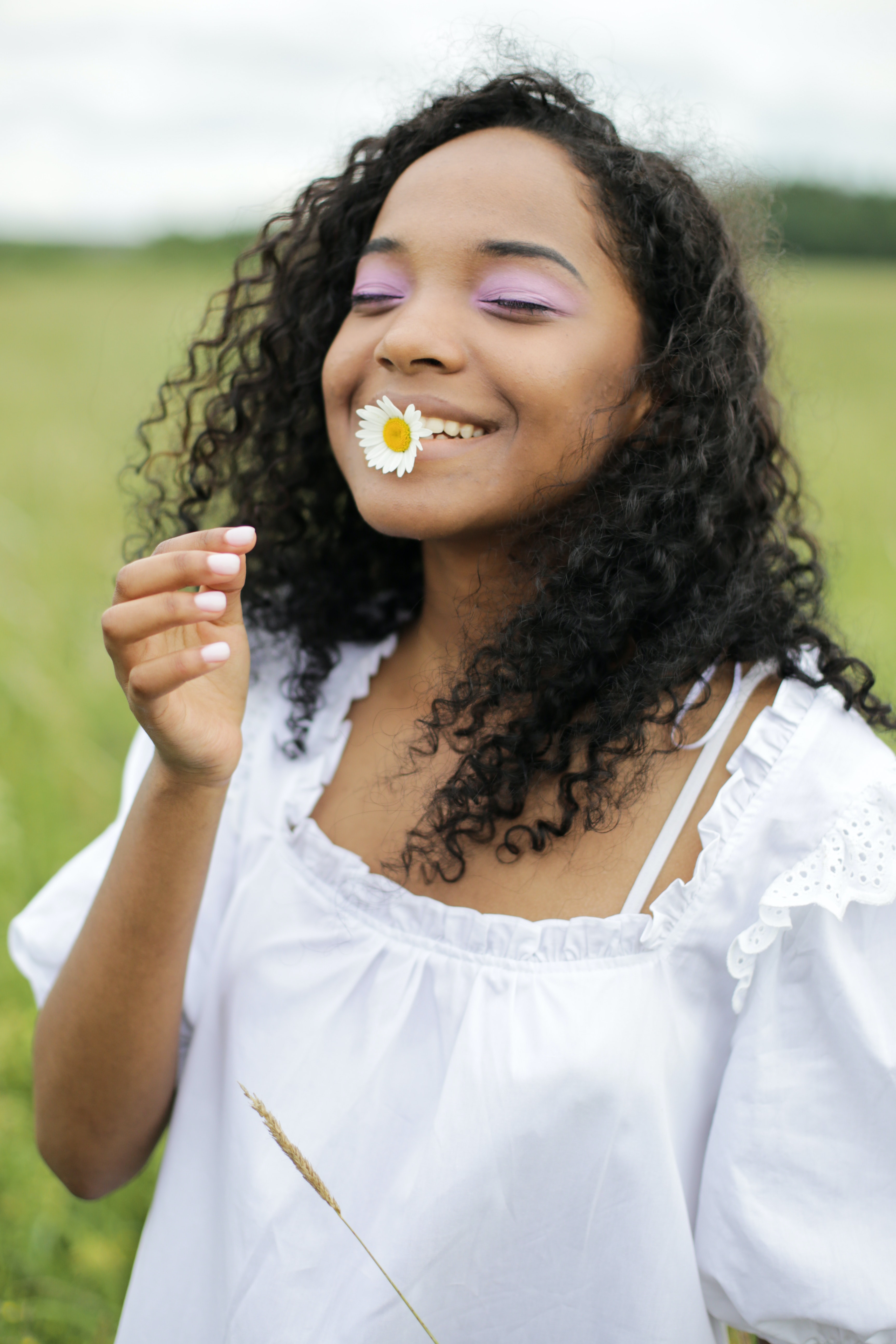 girl in a white dress in a field with white flower between her teeth